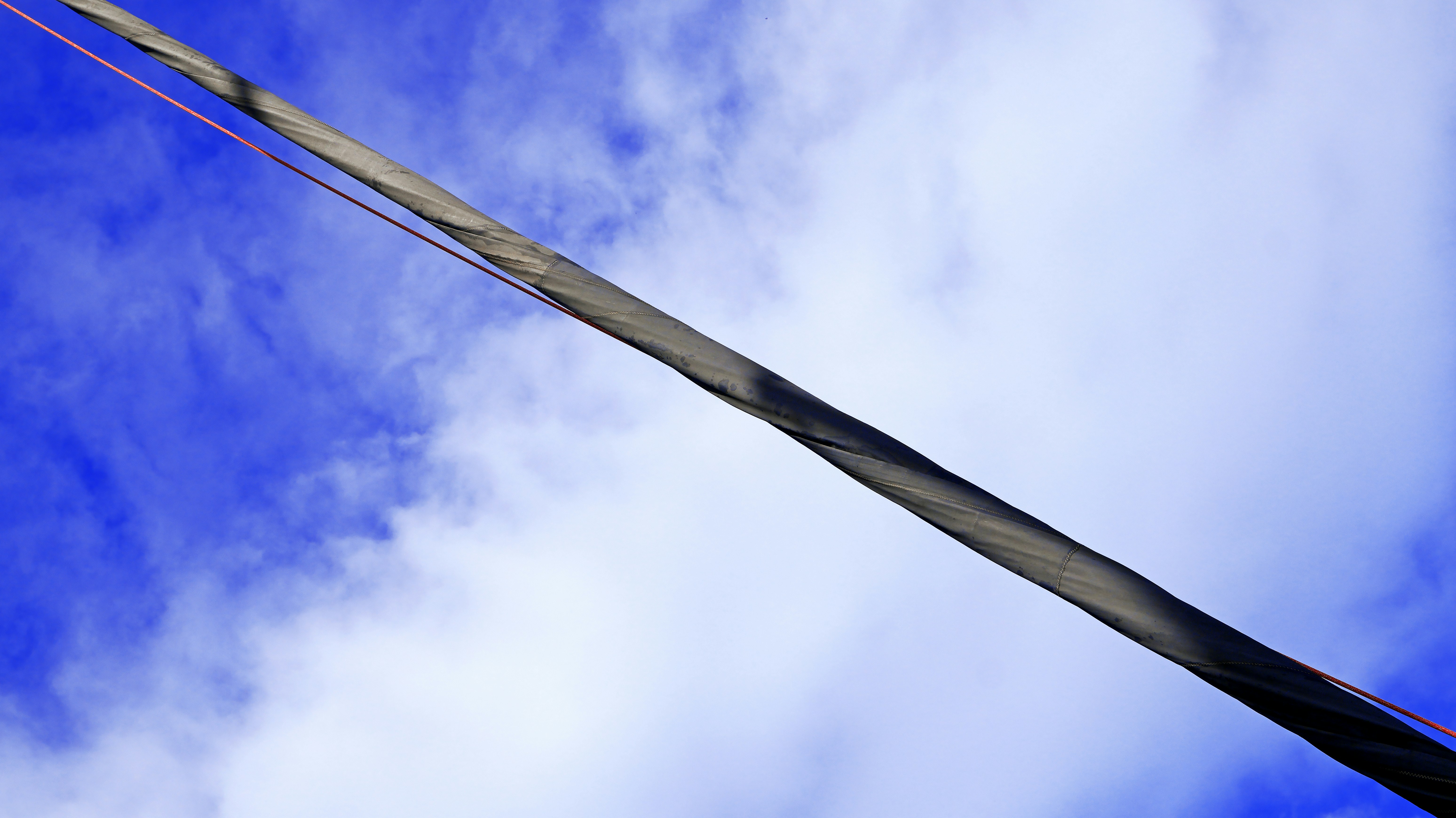 A diagonal sailboat mast against a bright blue sky with scattered white clouds