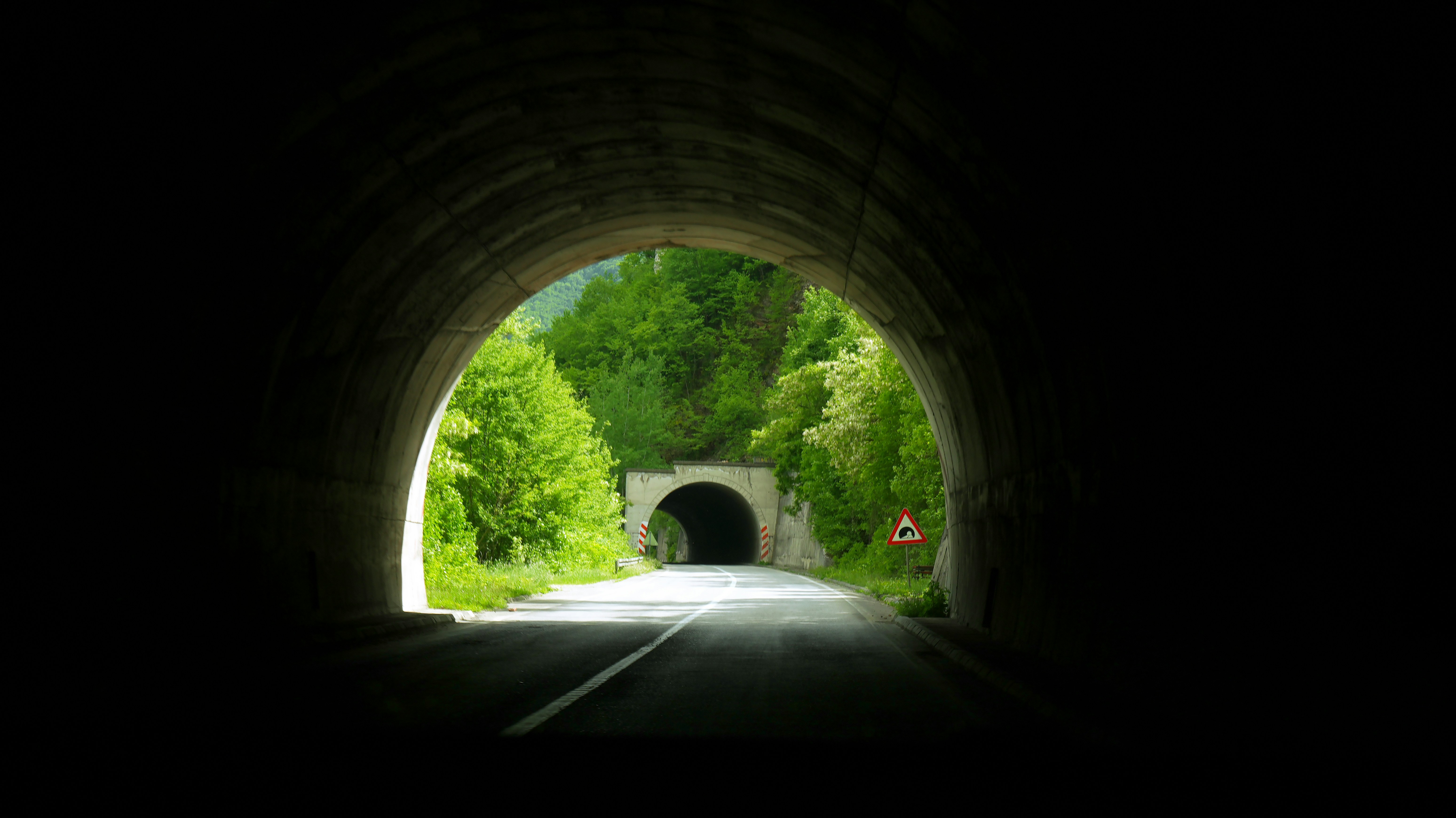 A view through a dark tunnel toward a sunlit road and another tunnel entrance