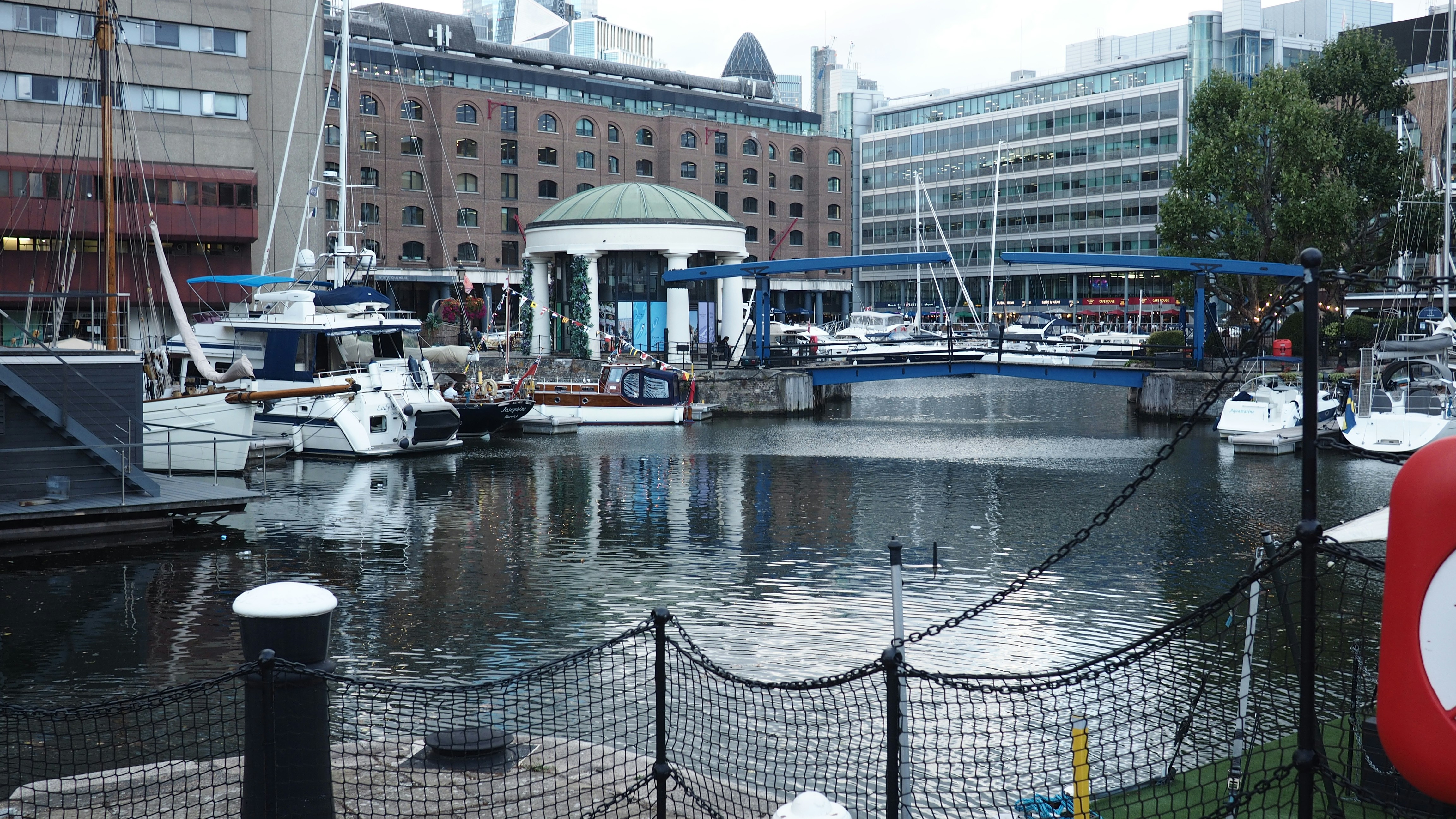 Boats moored in St Katharine Docks with a blue footbridge and city buildings in London