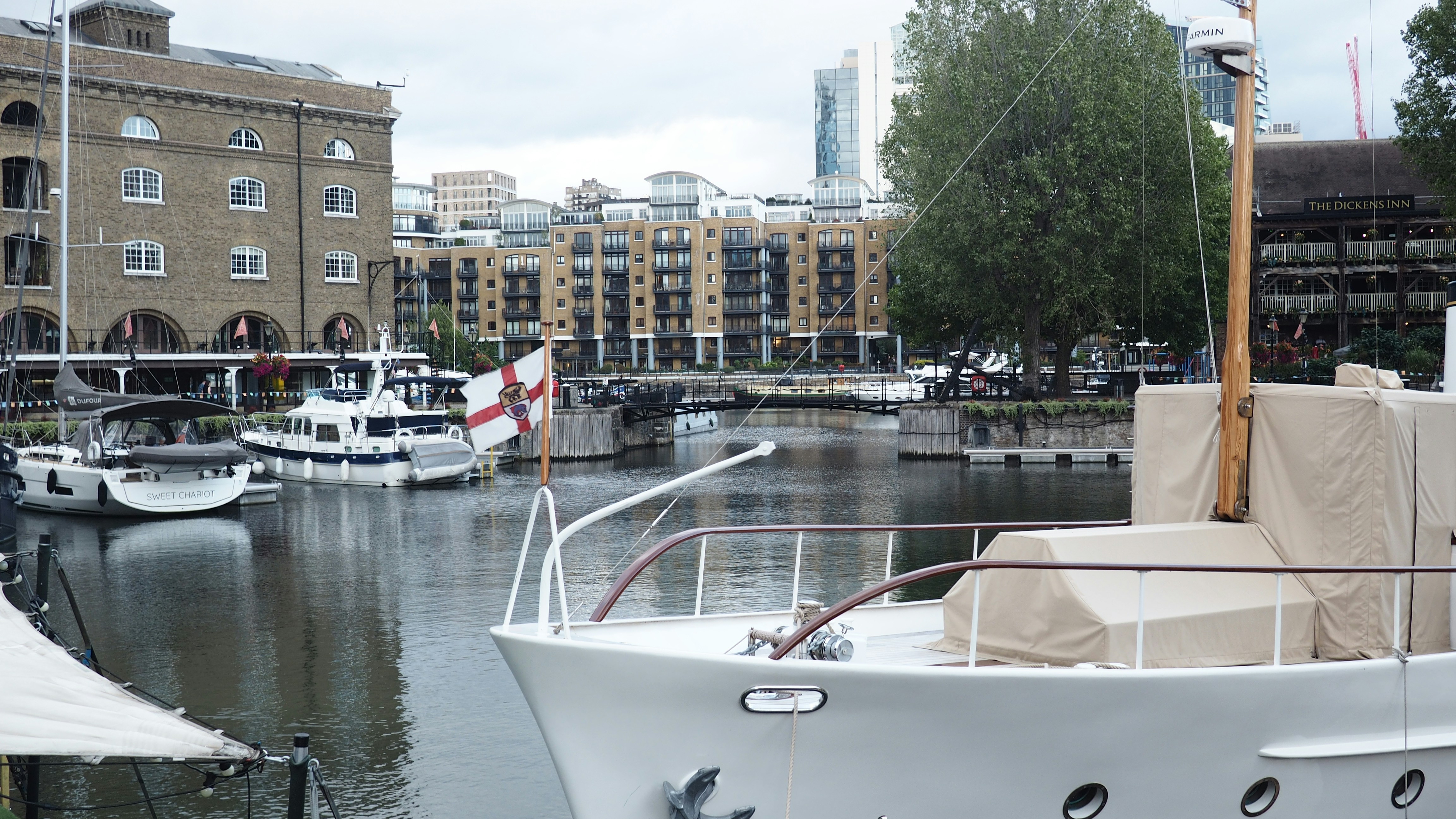 Boats moored in St Katharine Docks with brick buildings and The Dickens Inn in London