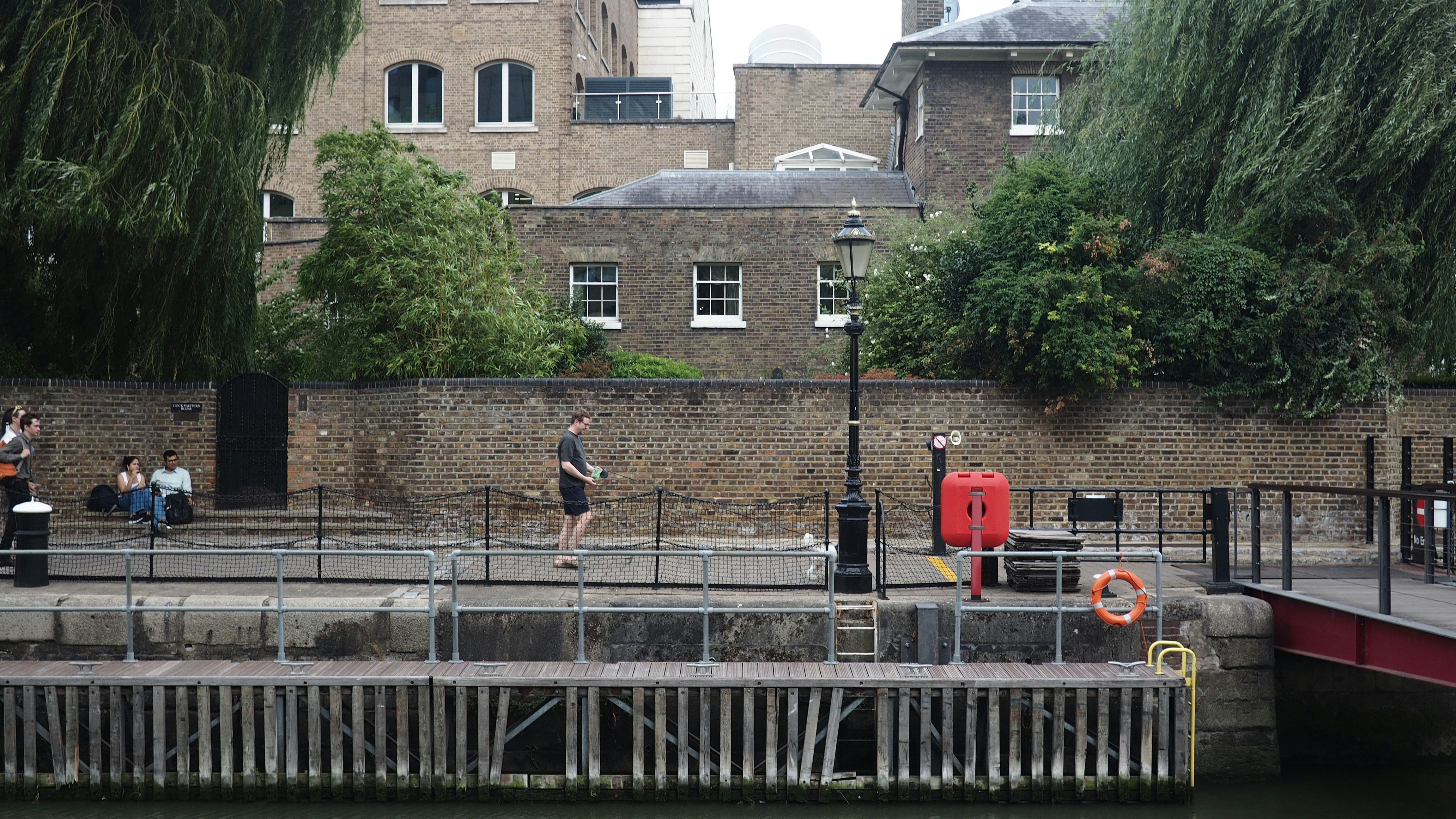 A person walking a small dog along a brick-walled canal path in London