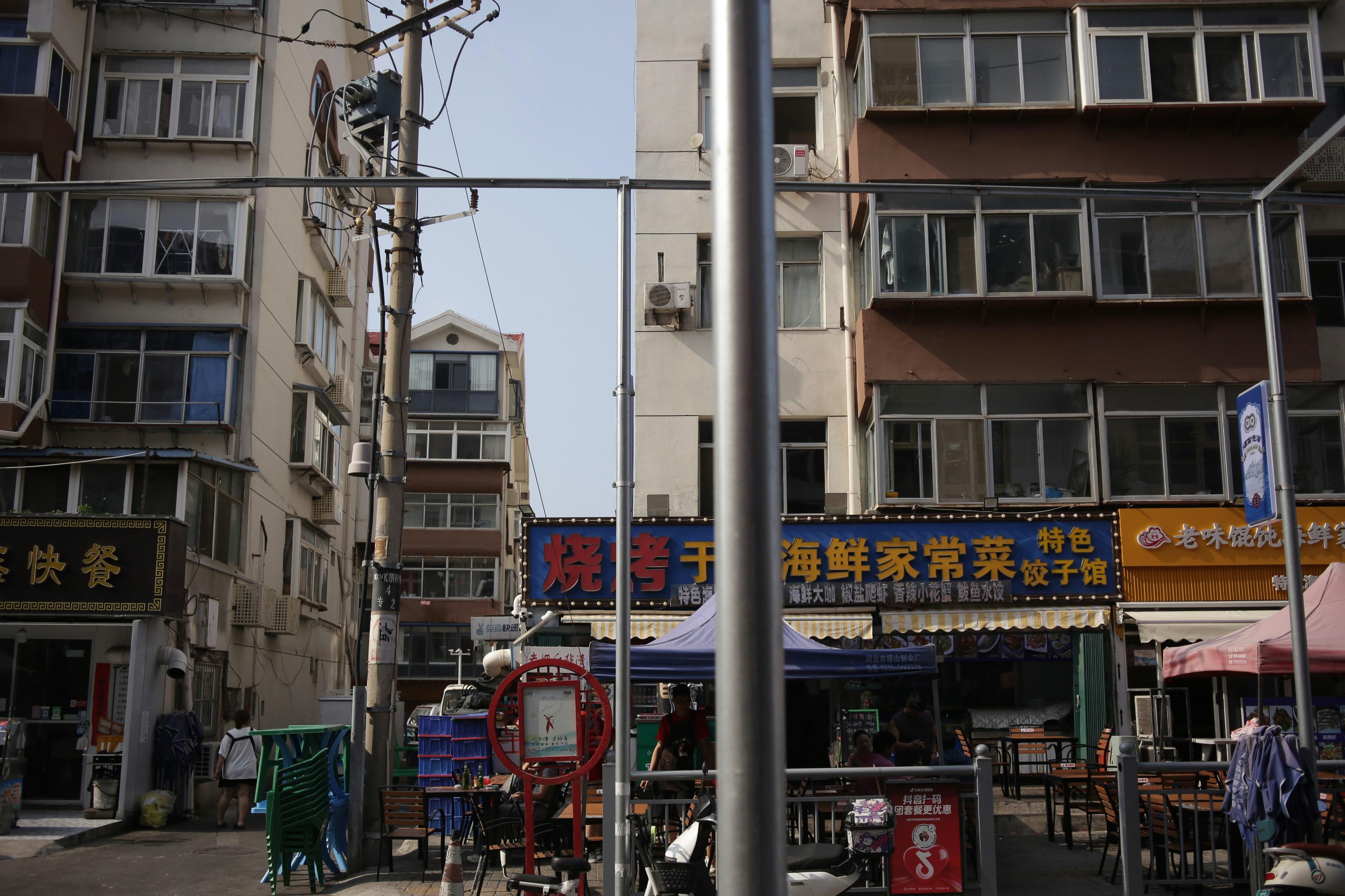A narrow street between residential buildings with storefronts and outdoor seating in a city