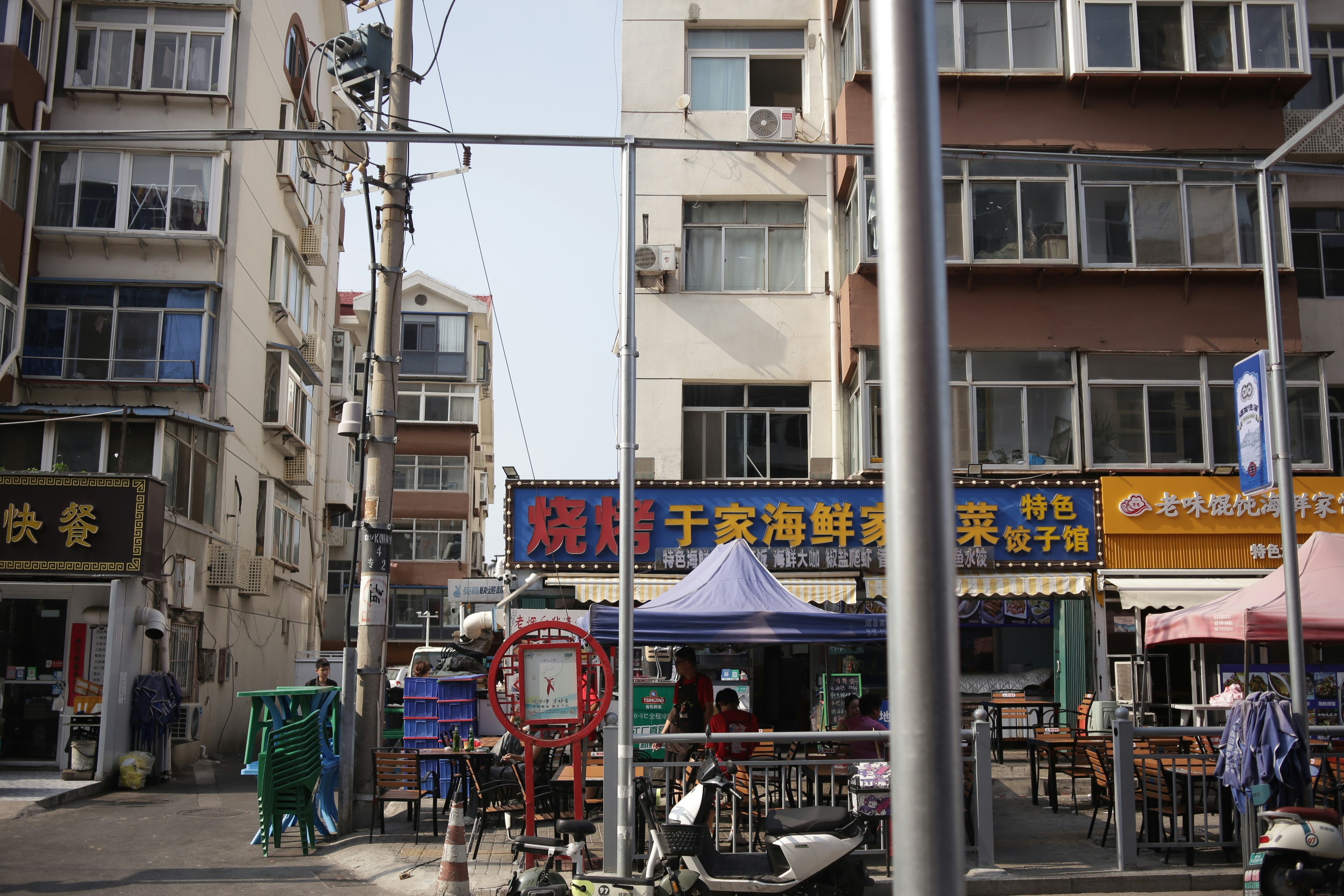 Outdoor seating at a restaurant with blue signage and a purple canopy on a city street