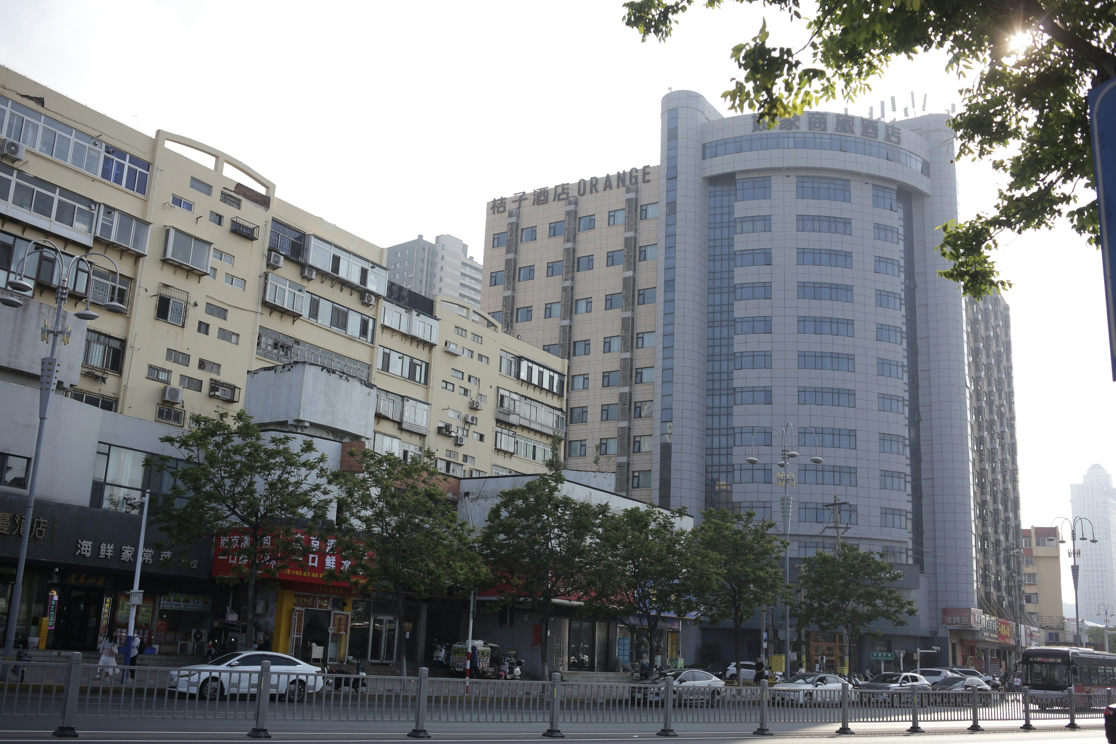 A busy city street with multi-story apartment buildings and a modern hotel under a bright sky