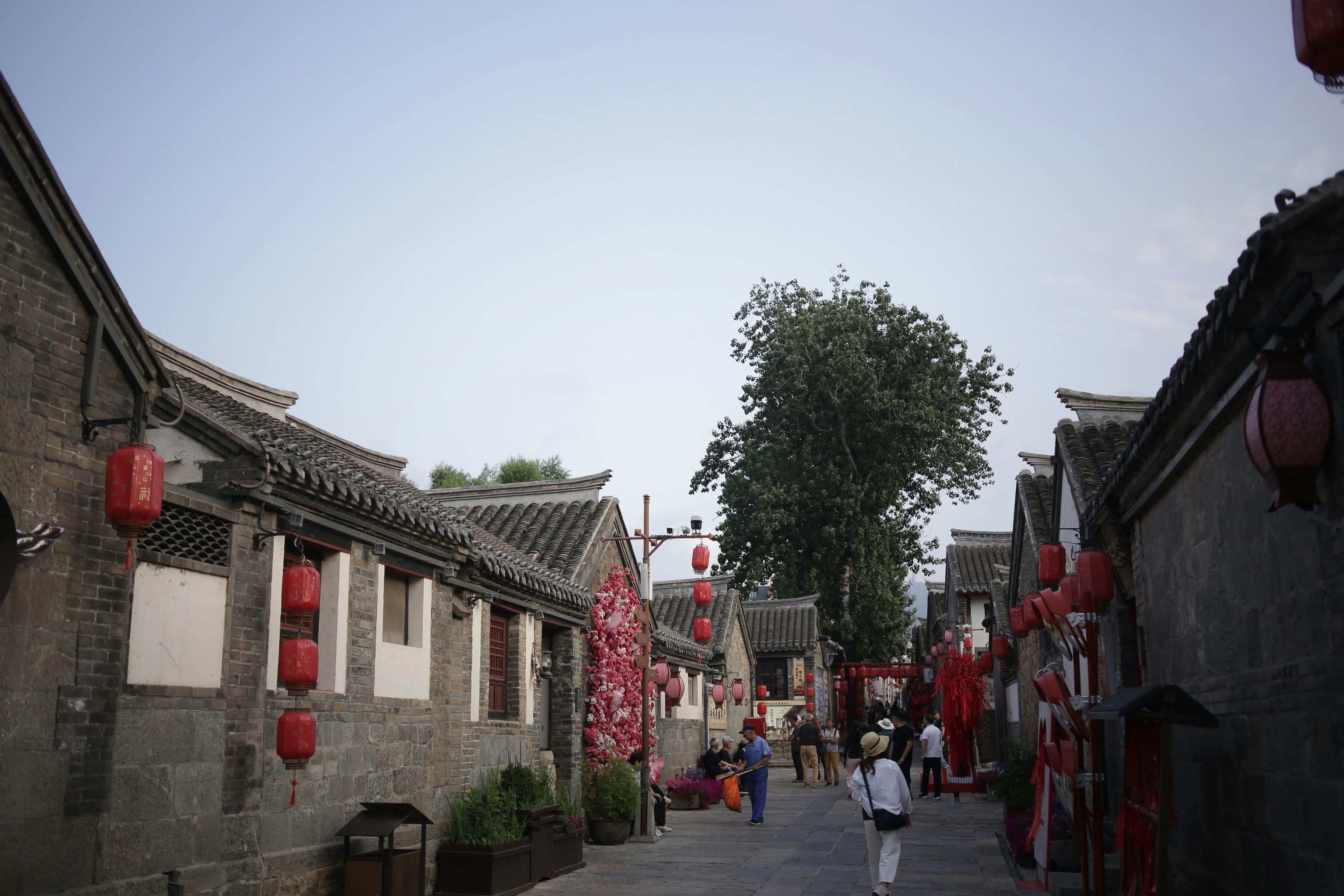 People walking along a narrow stone street lined with traditional buildings and red lanterns
