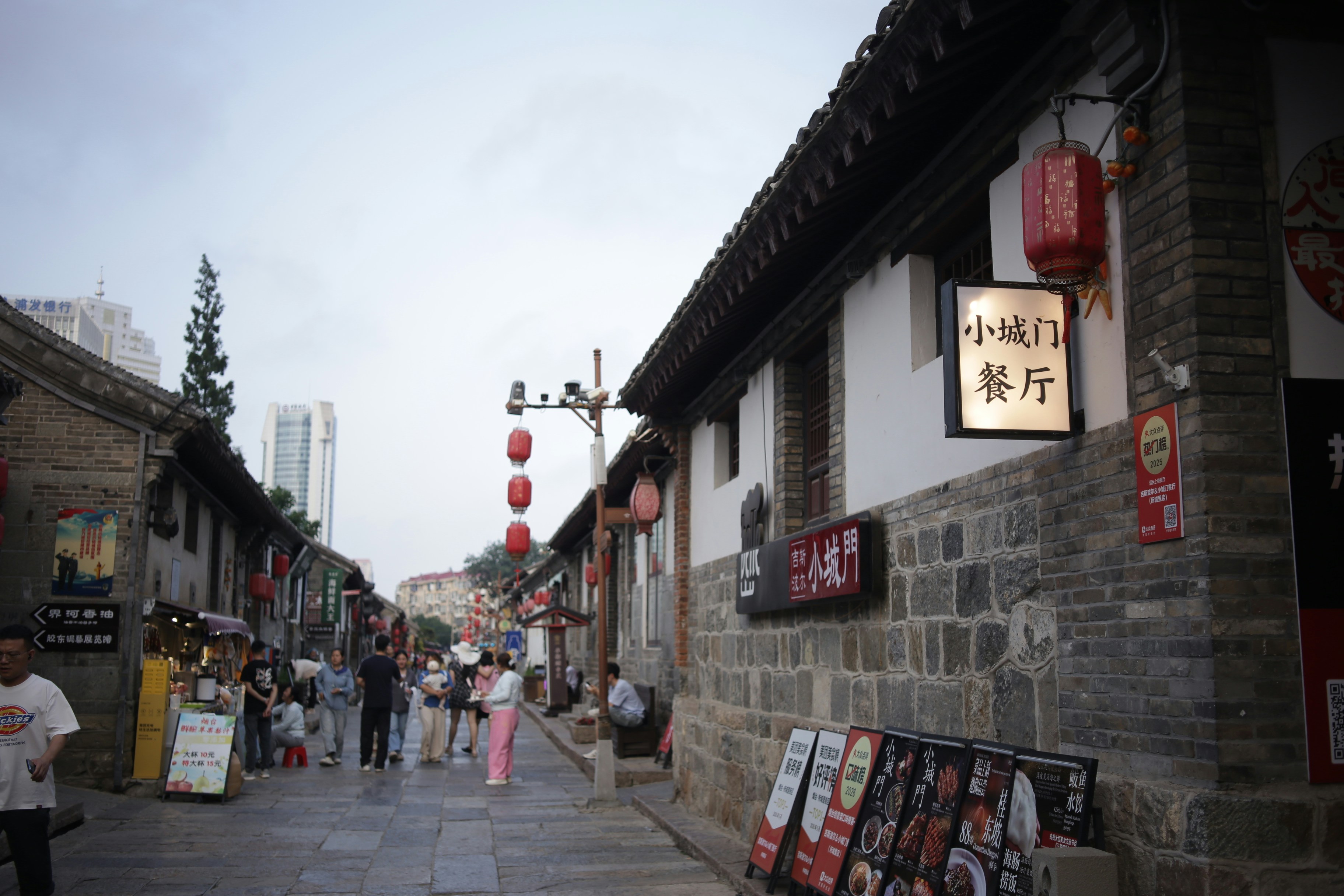 People walking along a stone-paved street lined with traditional buildings and red lanterns in China