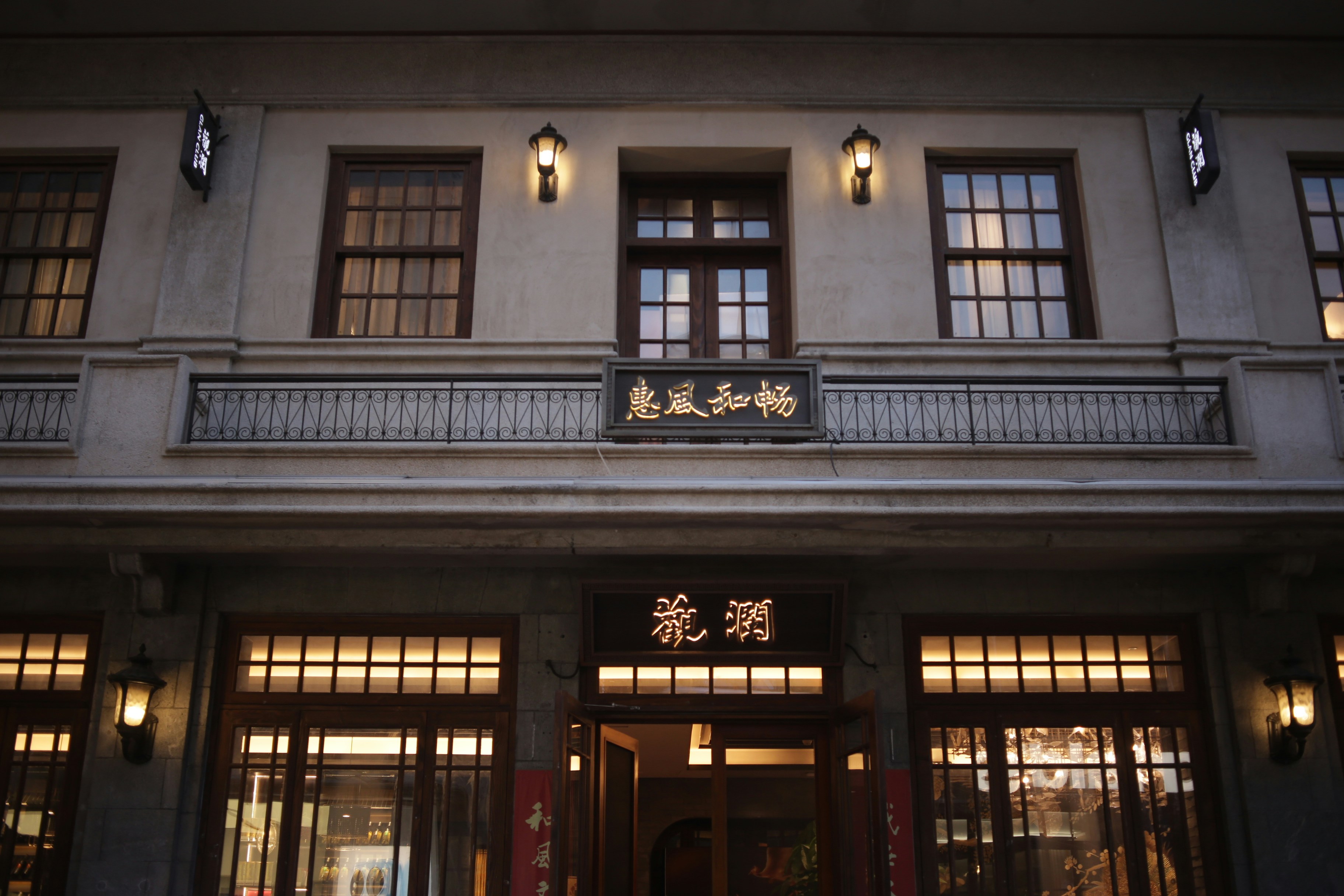 A two-story building with illuminated Chinese signage and warm wall lamps at night