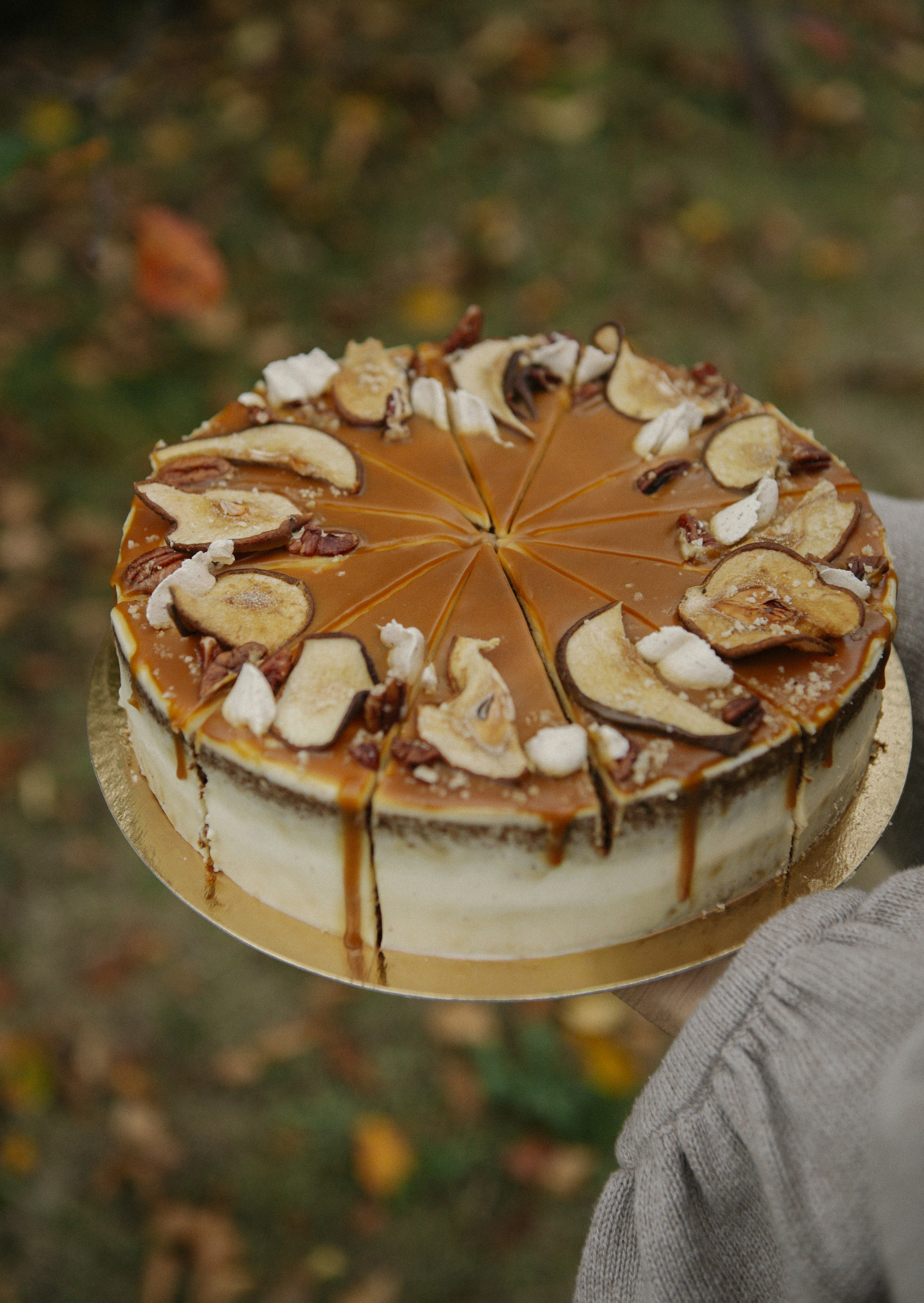 A sliced caramel cake topped with dried apple slices and pecans held in a hand