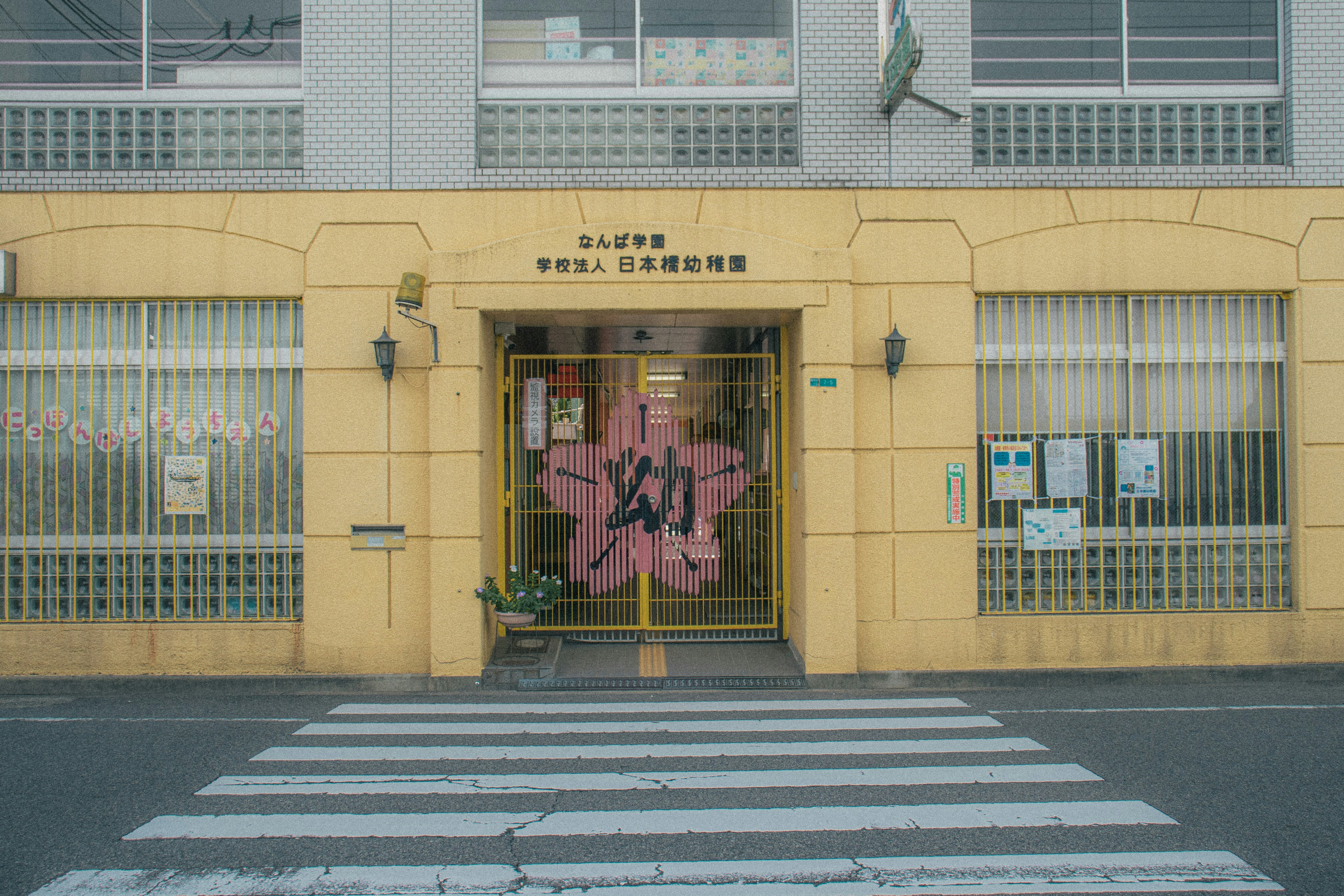 黄色い学校の建物で、ゲート付きの入口と前景に横断歩道があります