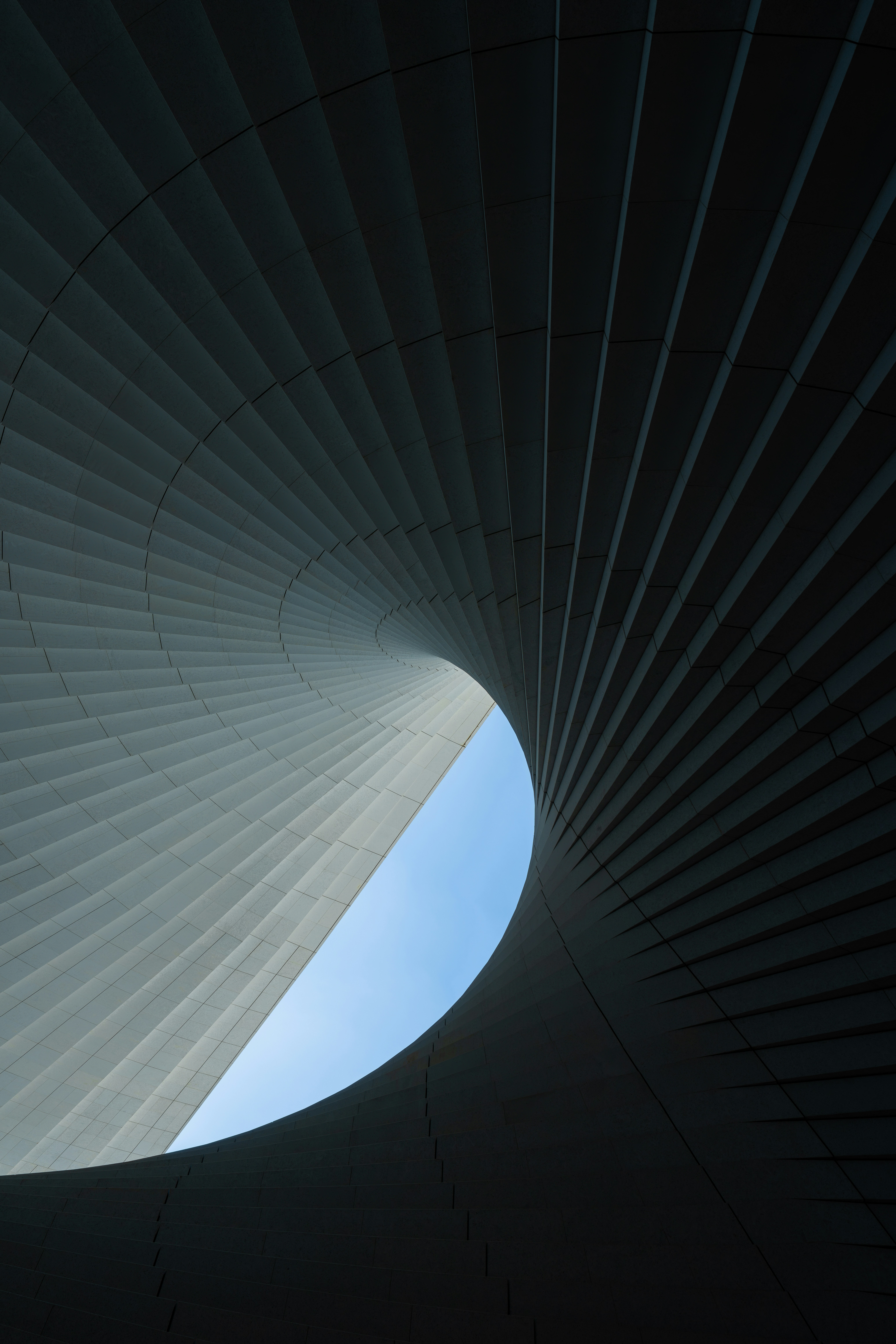A 3D render of a spiraling architectural structure with curved panels framing a sliver of blue sky