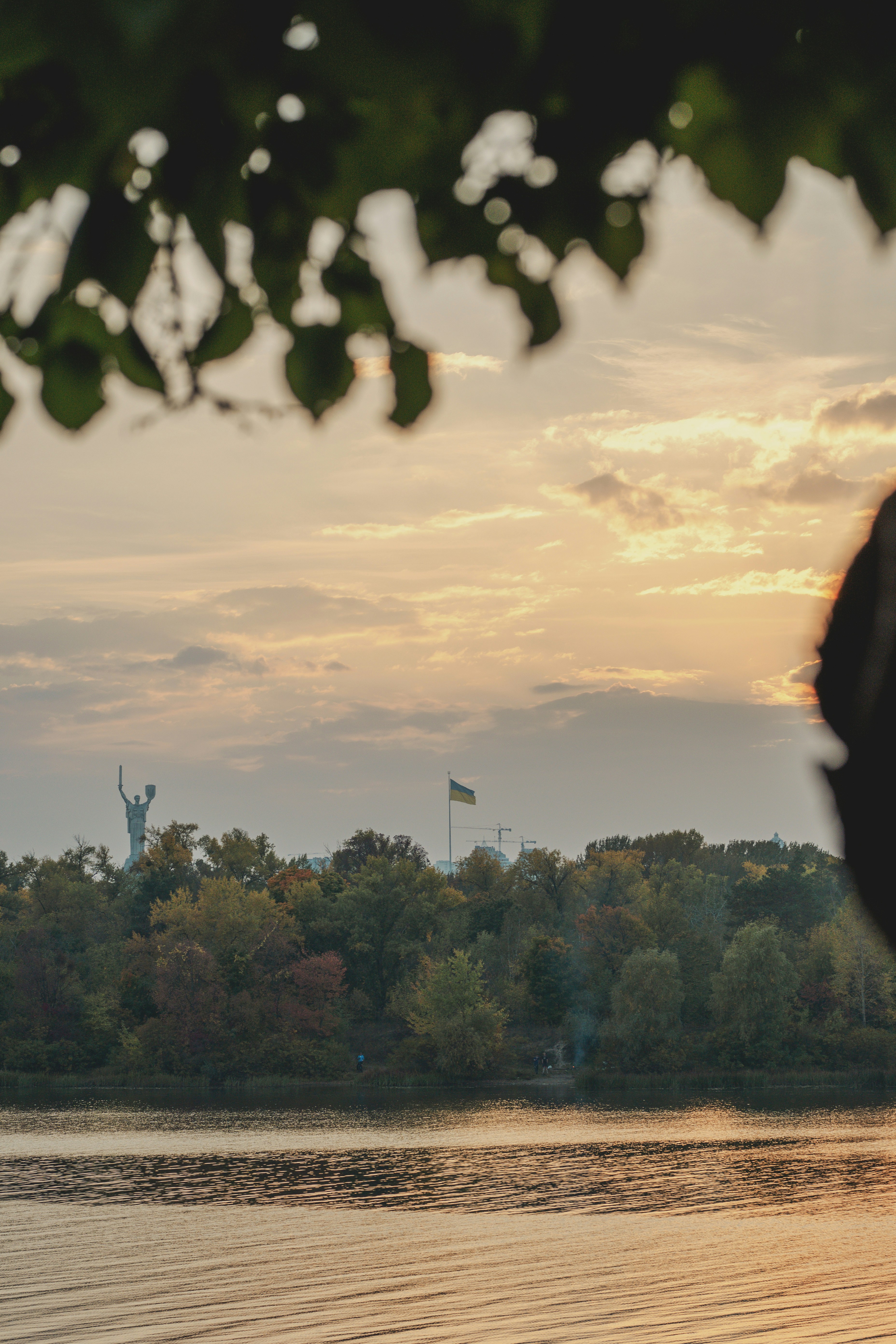 Das Mutterlanddenkmal und eine ukrainische Flagge über den Herbstbäumen am Dnepr in Kiew
