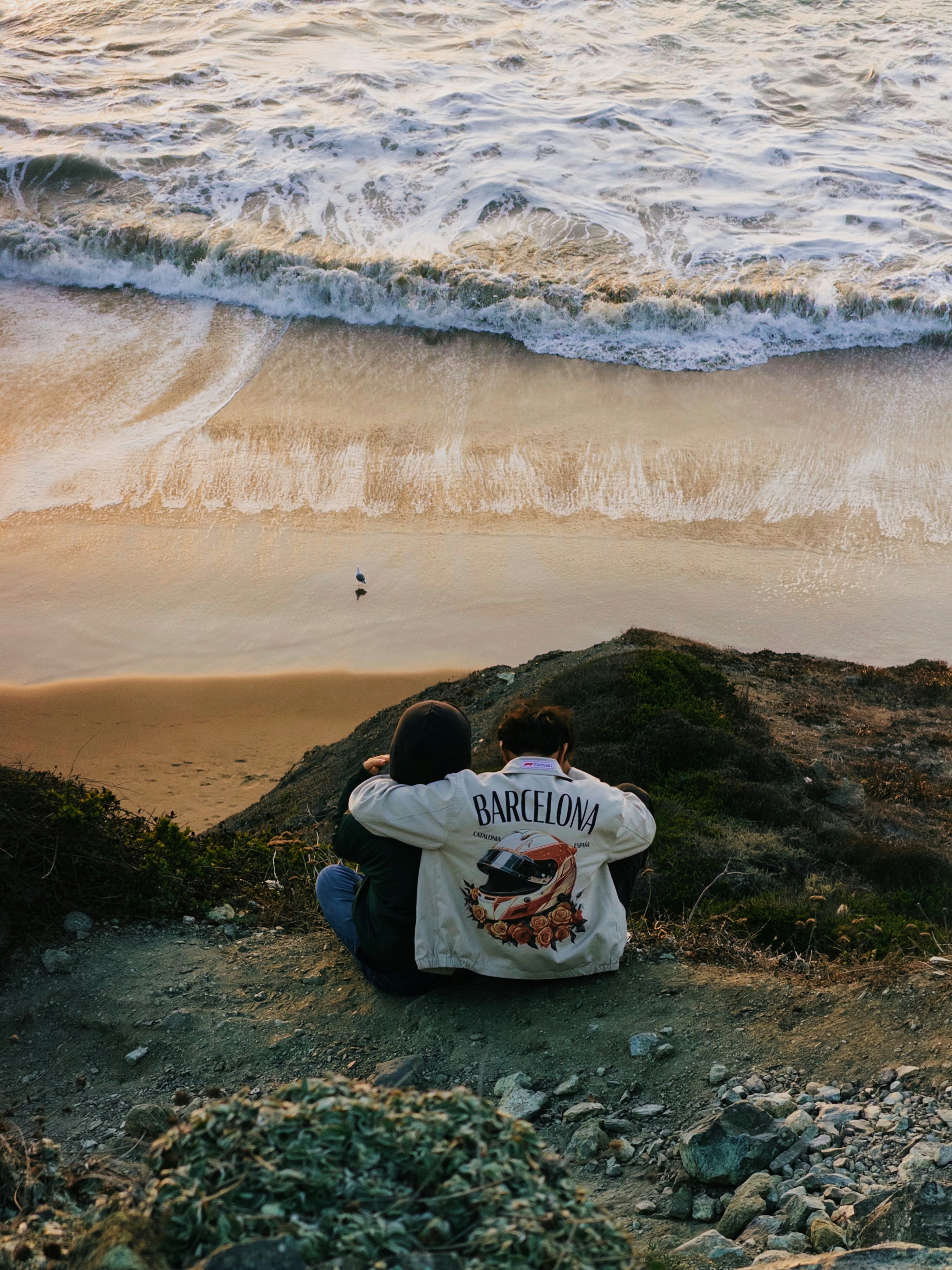 Two people sitting on a cliff overlooking the ocean at golden hour