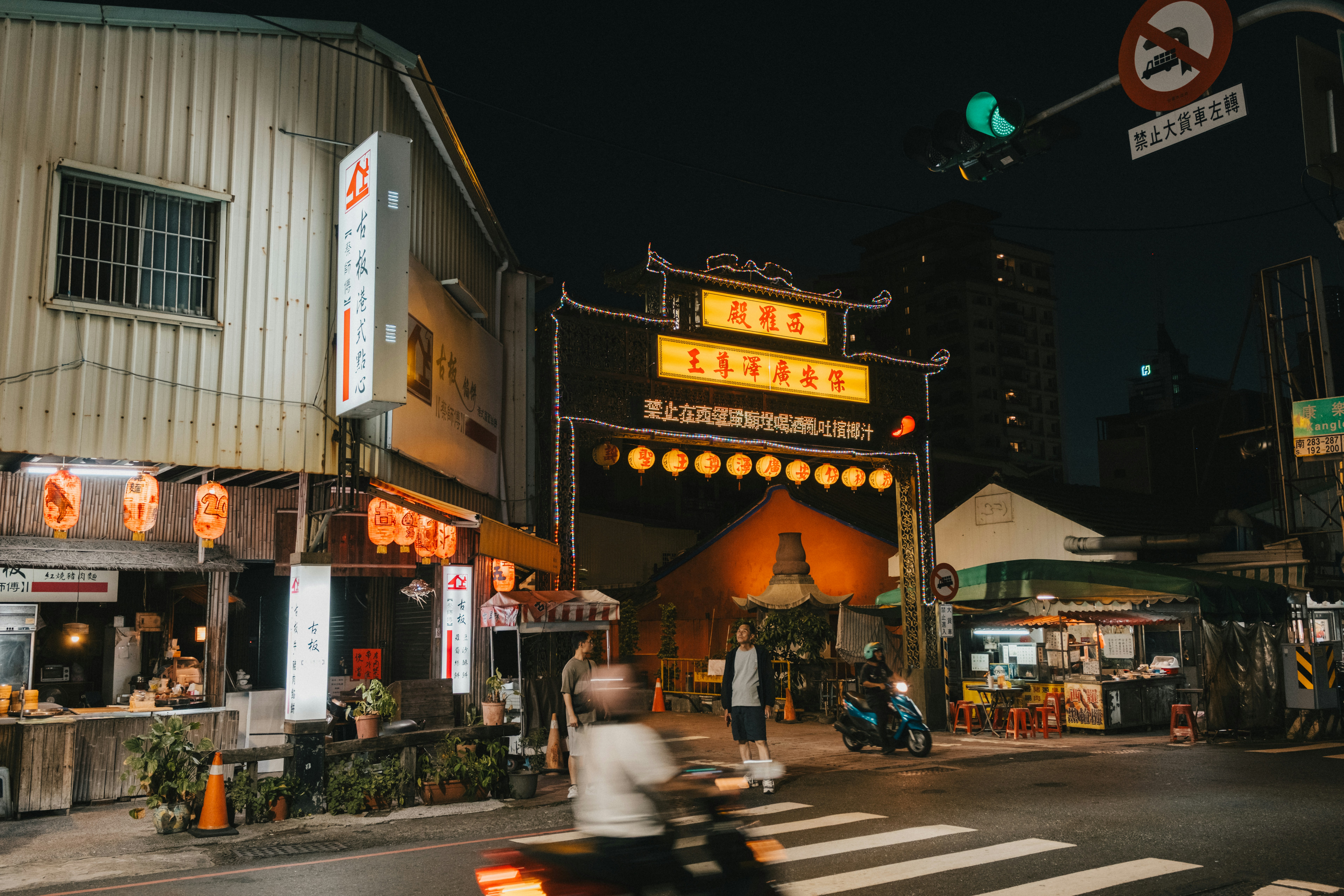 Una persona de pie junto a una puerta tradicional con faroles y carteles encendidos por la noche en Tainan