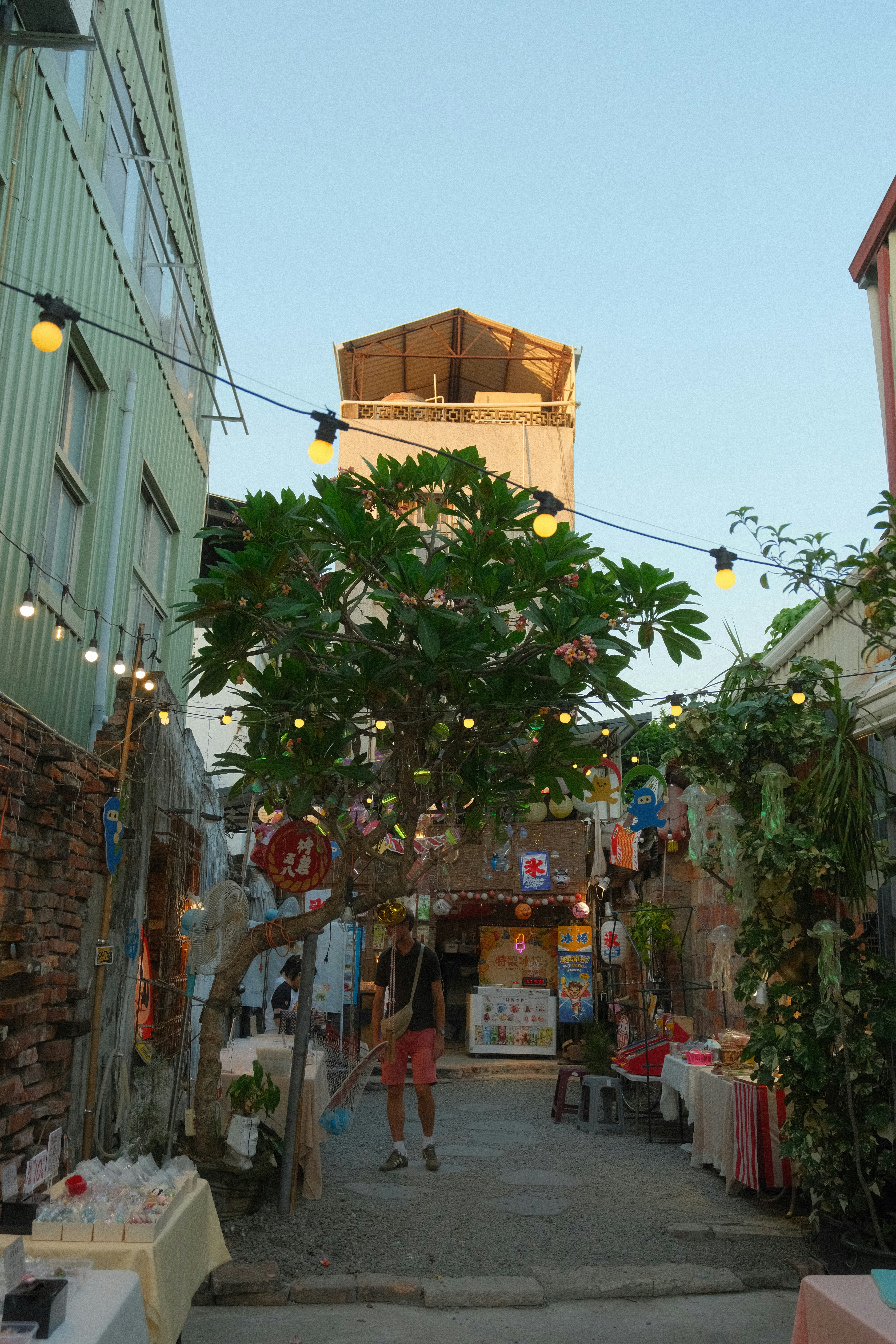 Una persona caminando por un callejón estrecho decorado con luces de hilo y pequeños puestos de mercado