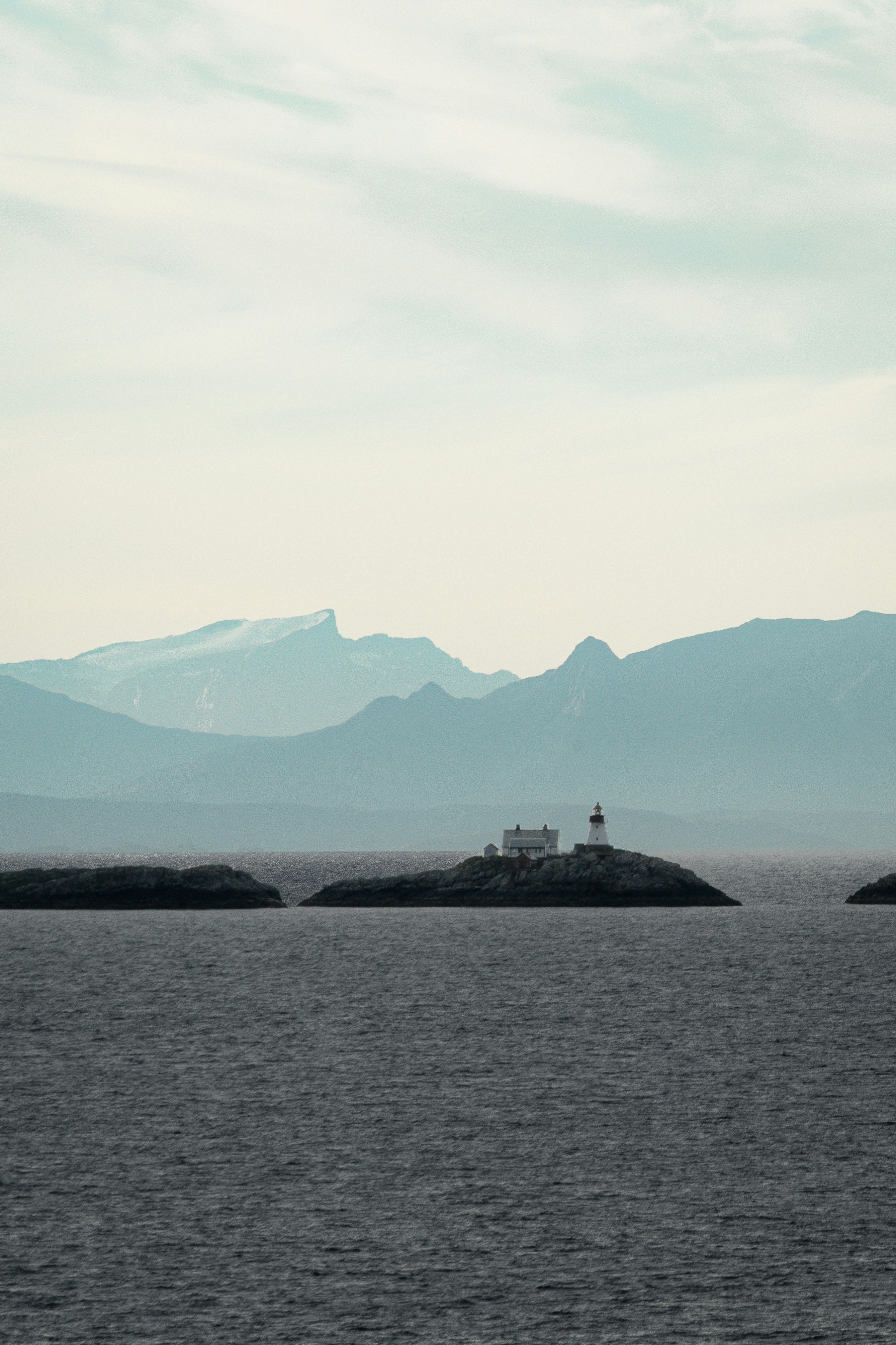 Un faro e una piccola casa su un'isola rocciosa davanti a lontane montagne blu