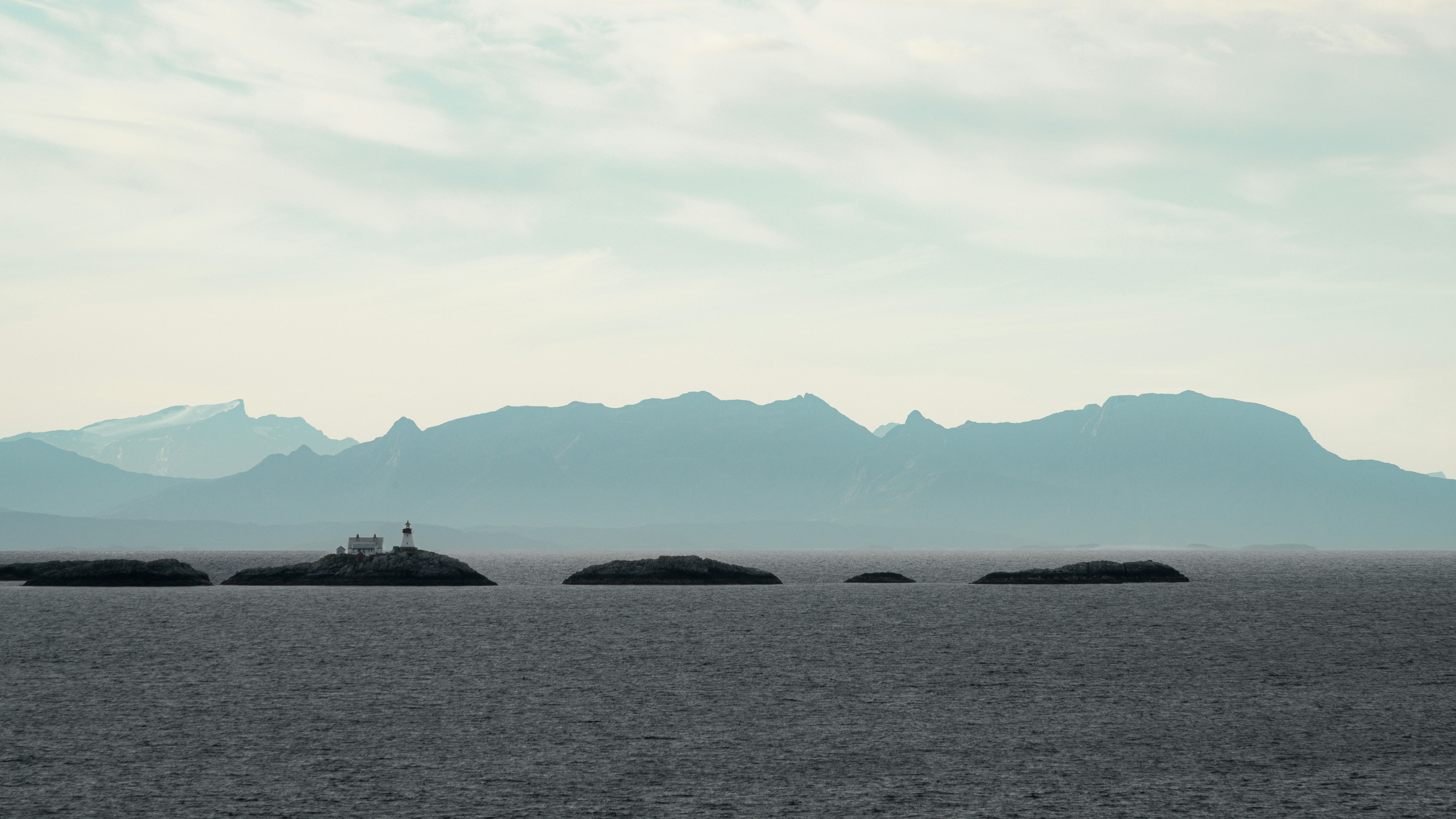 Un piccolo faro su un'isola rocciosa nel mare davanti a lontane montagne blu