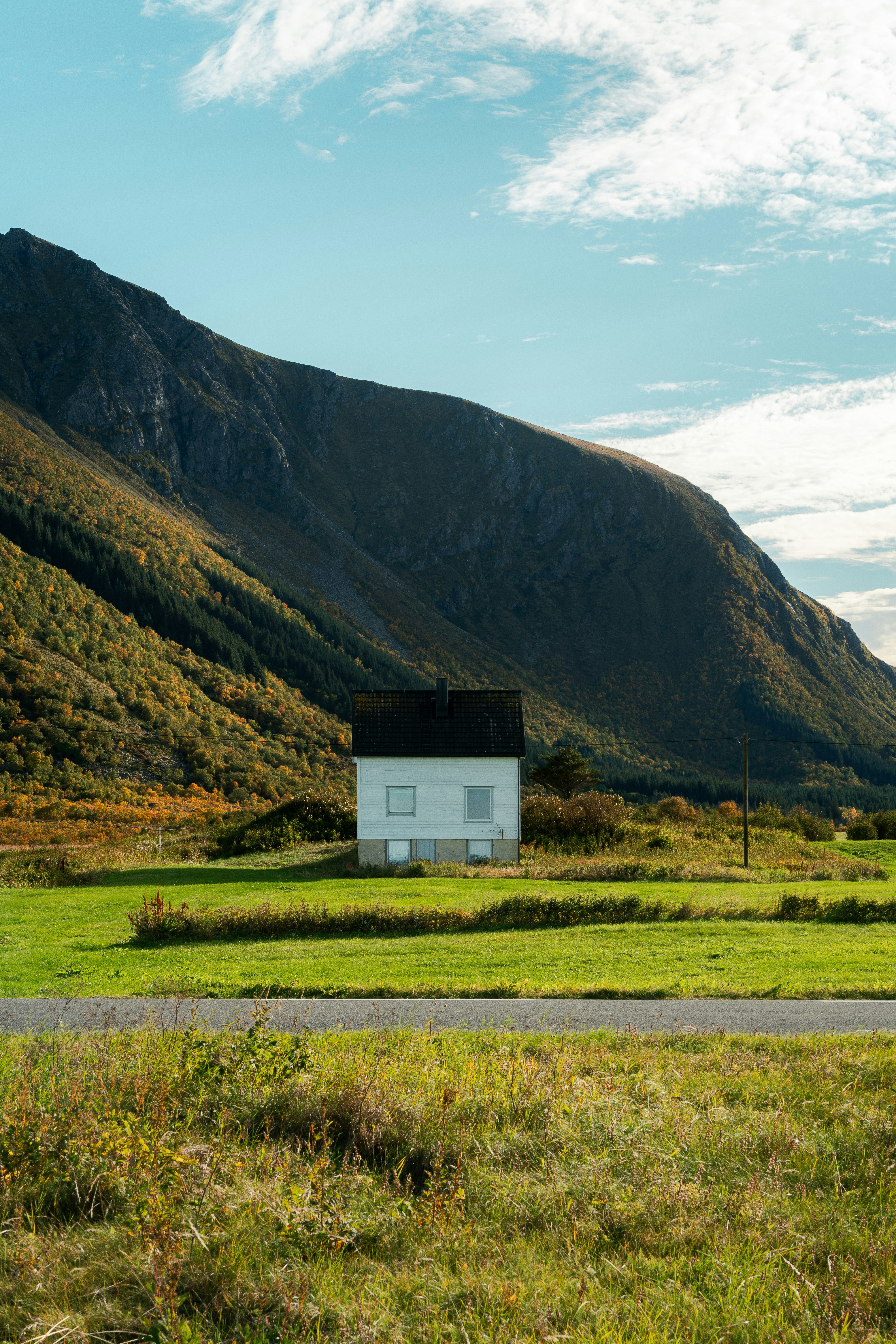Una casa bianca in un campo verde sotto una grande montagna con fogliame autunnale
