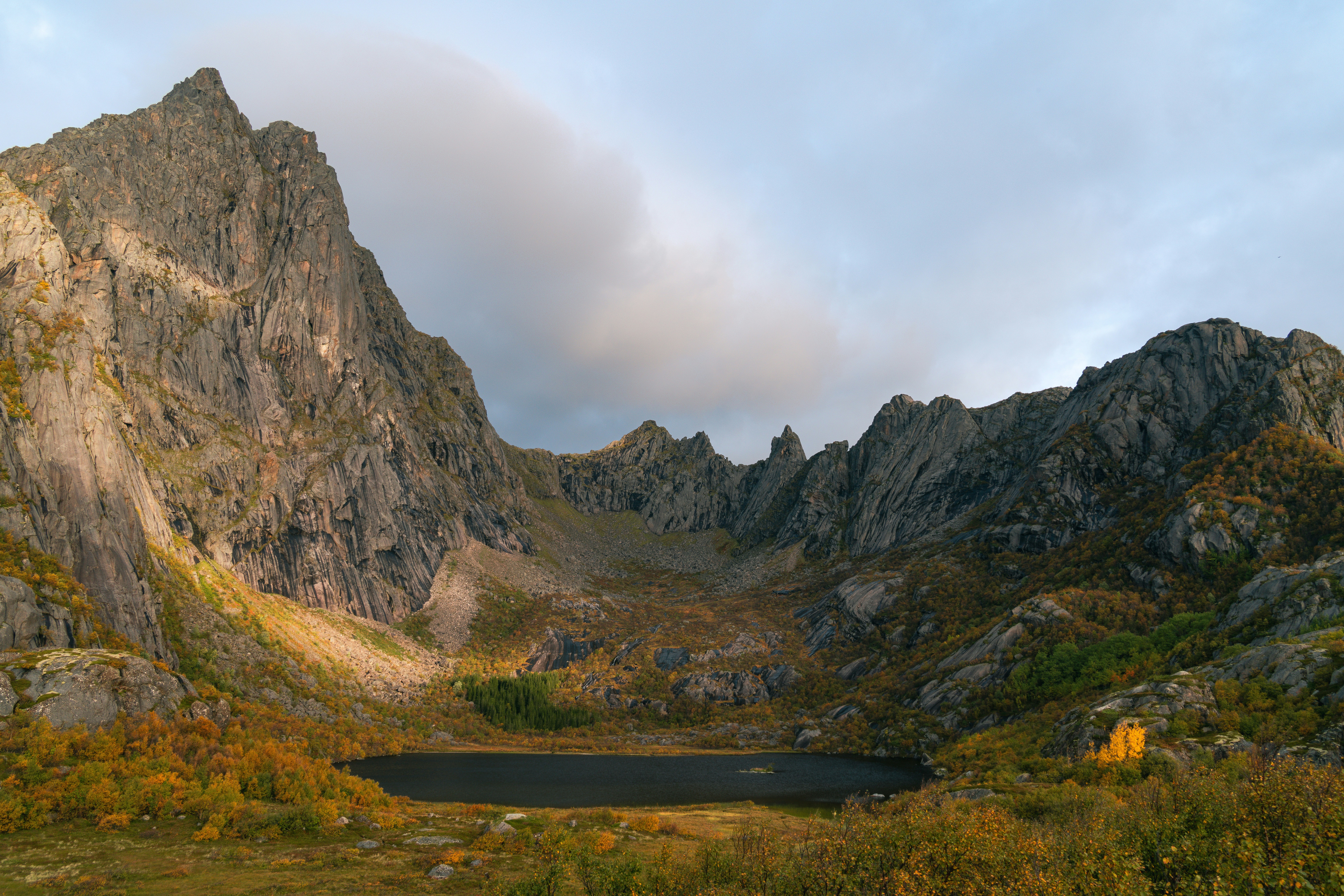 Un lago di montagna scuro incastonato in un circo roccioso con fogliame autunnale sui pendii