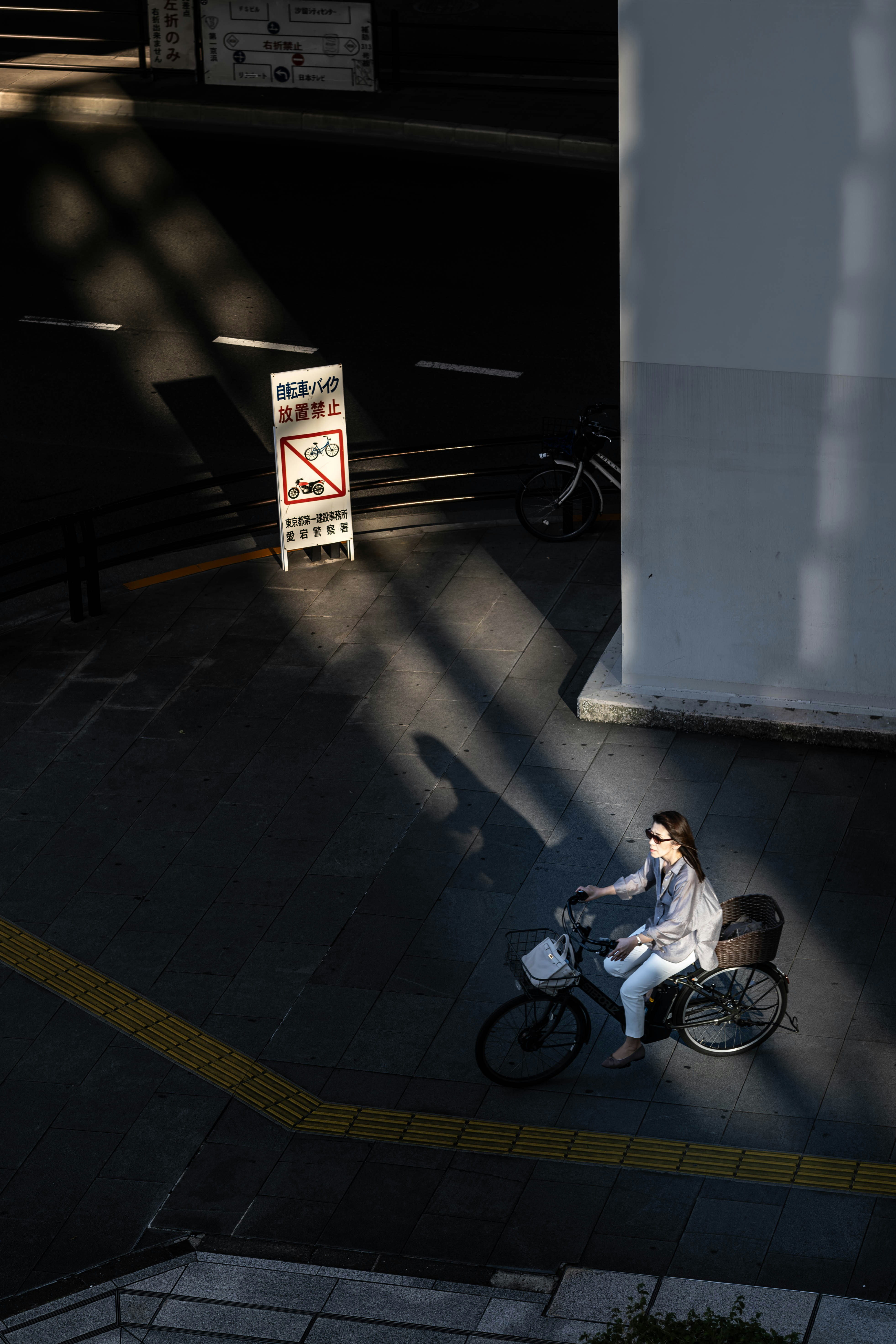 A woman cycling on a city street past a no-parking sign in Tokyo