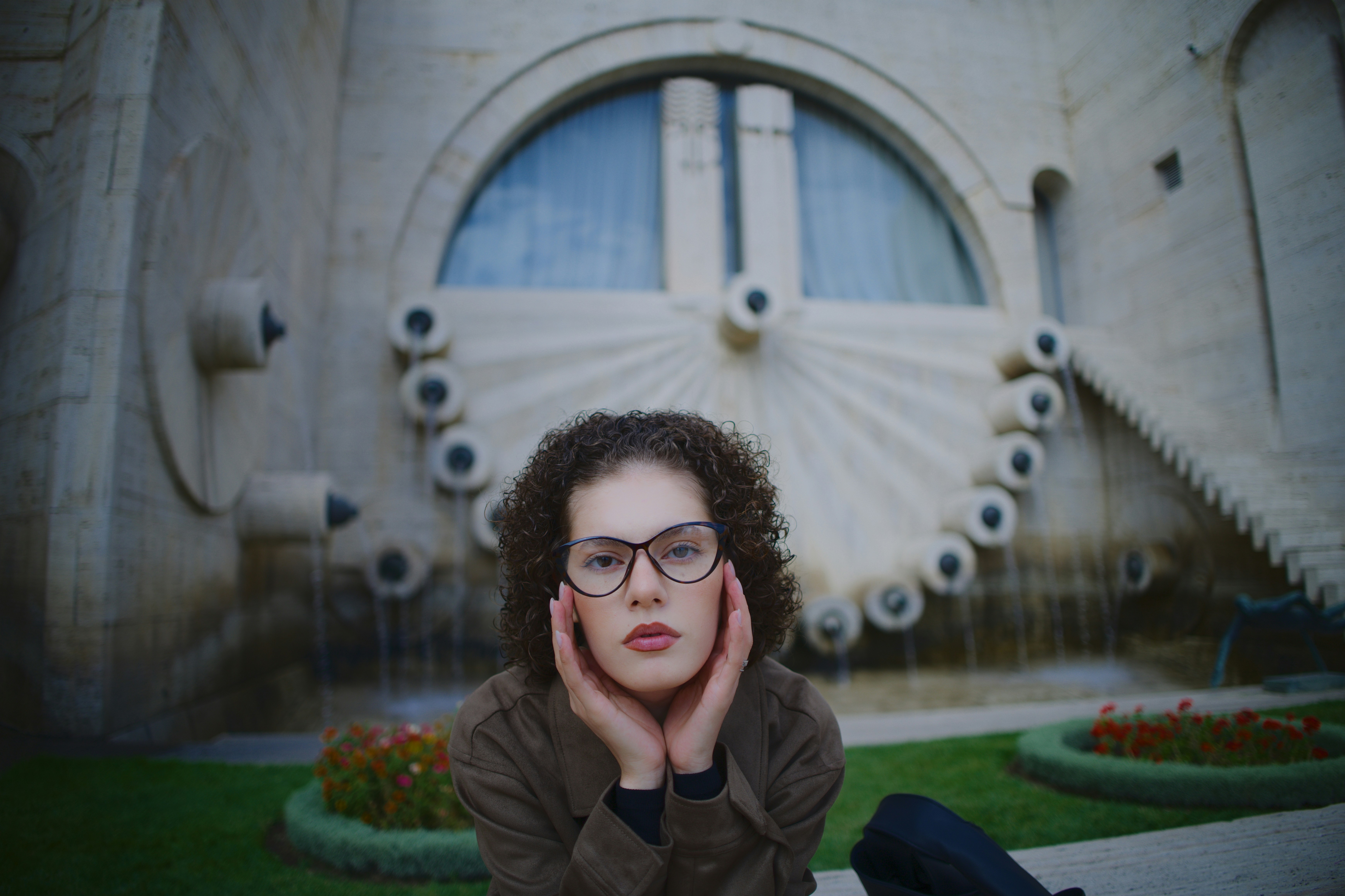 Una persona con el pelo rizado y gafas posando ante una gran fuente de piedra