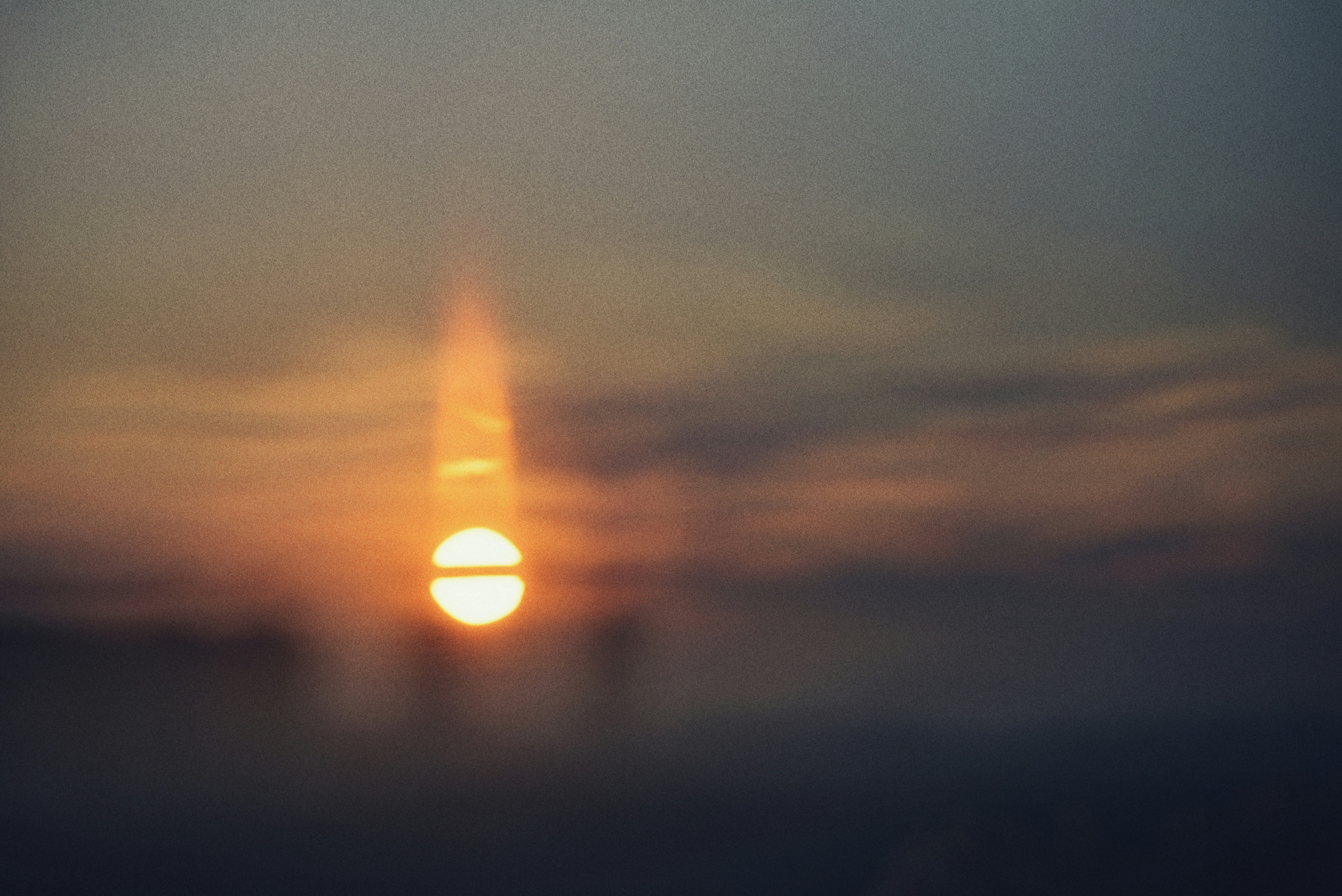 Un soleil bas et éclatant avec une lumière verticale s’éclipse dans un ciel orange brumeux