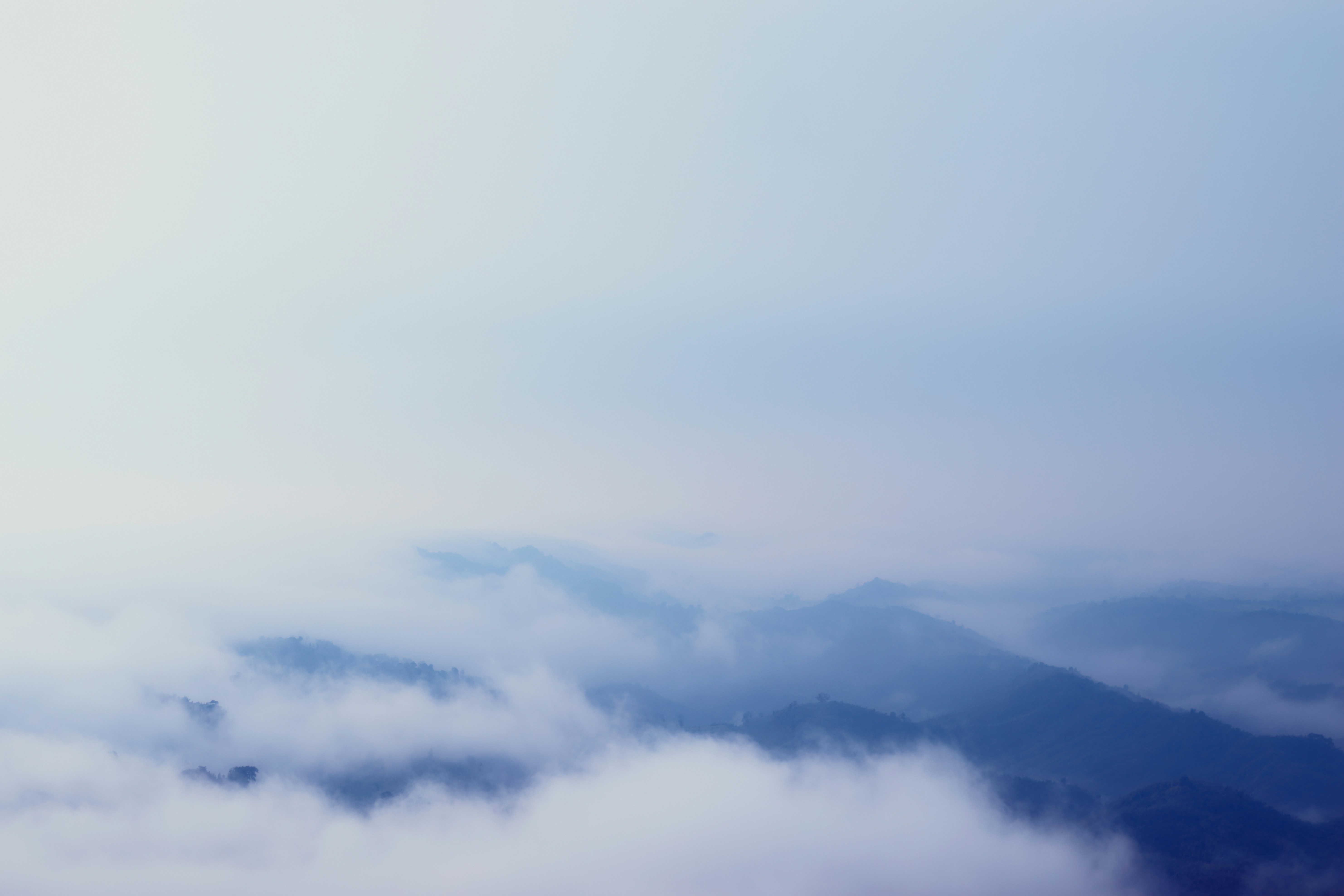 Blaue Bergrücken, die durch eine dicke Schicht Morgennebel auftauchen.