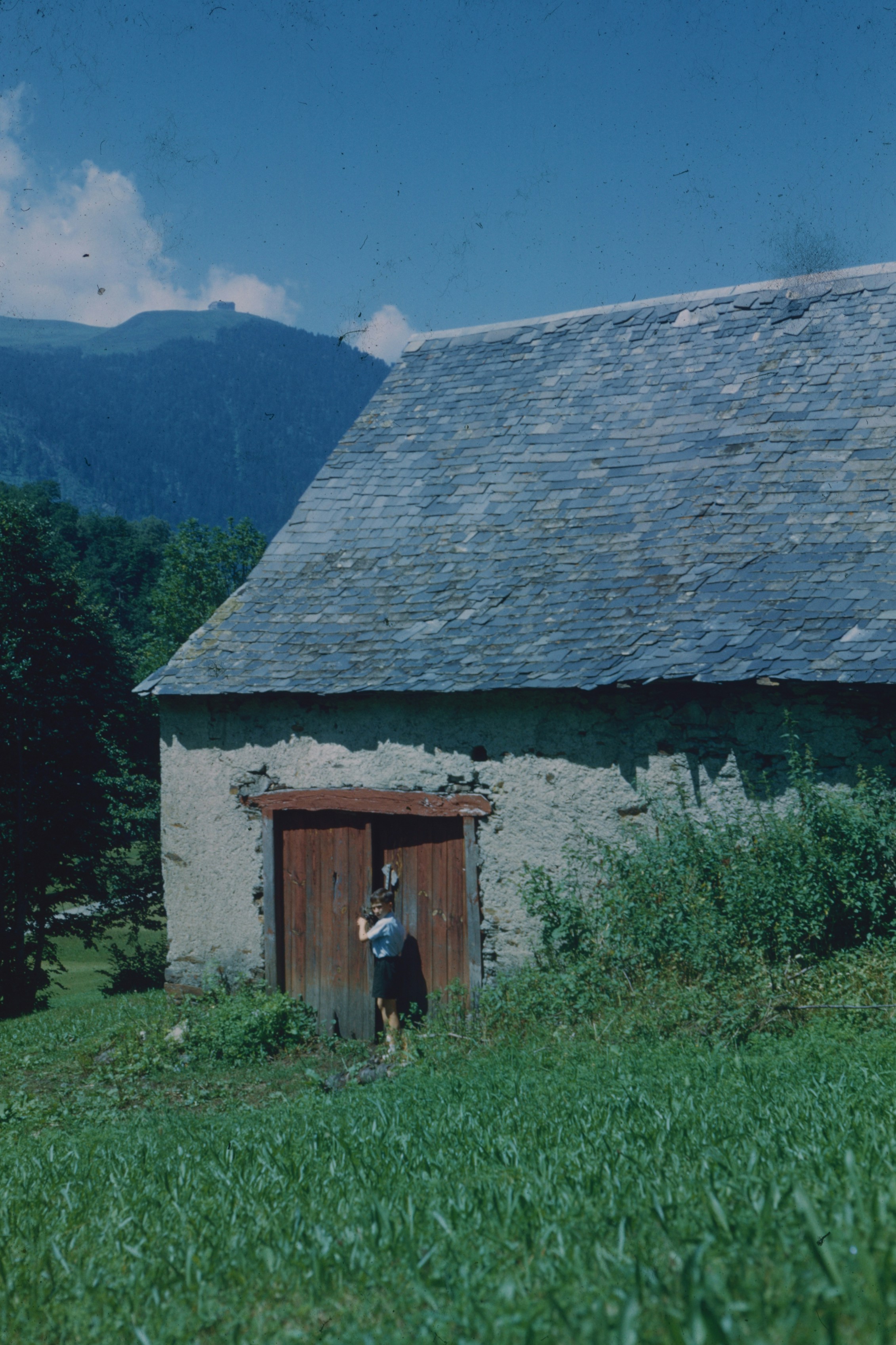 A child standing by the wooden doors of a stone barn in a mountain landscape