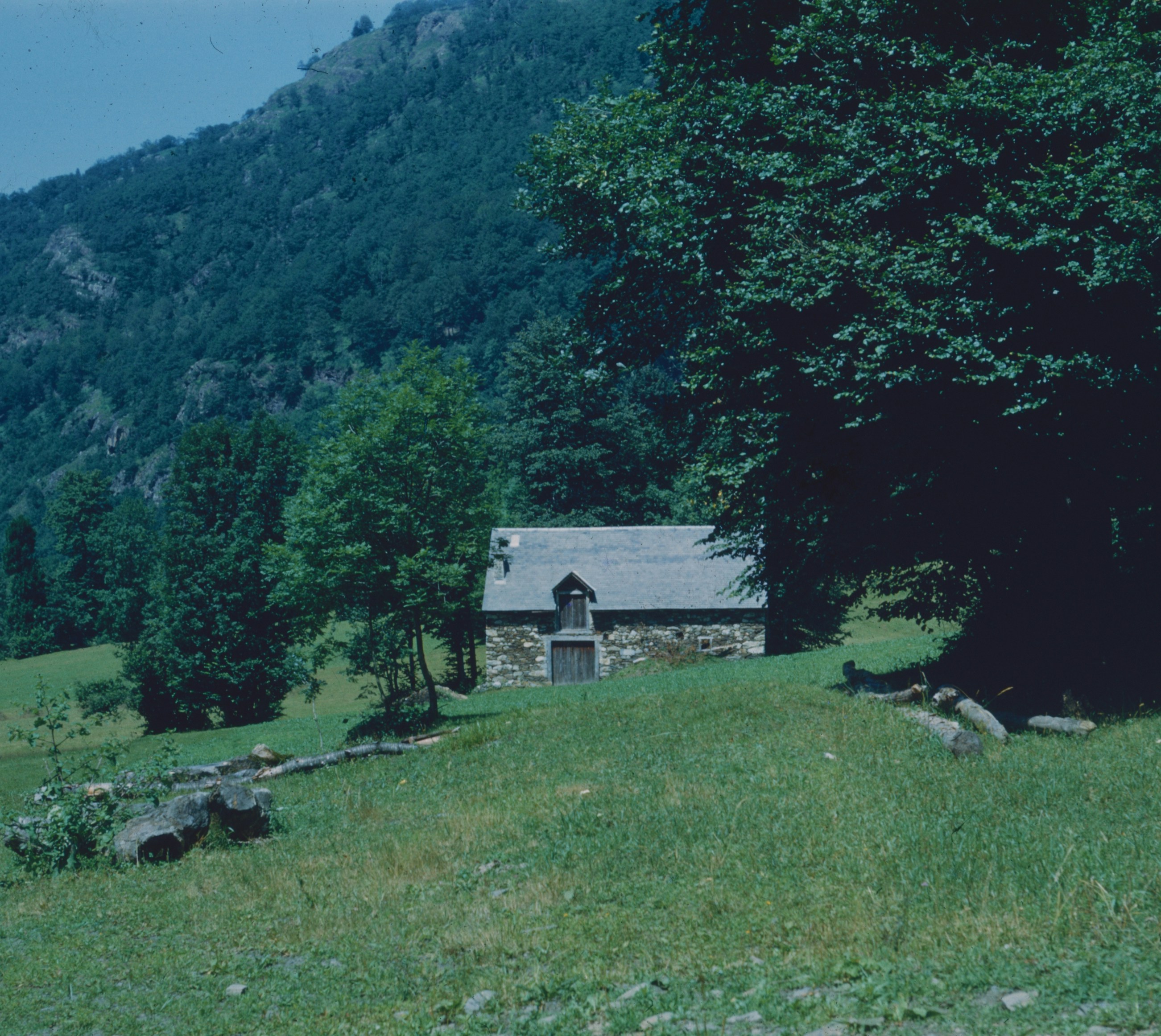 A stone barn with a slate roof in a green mountain meadow