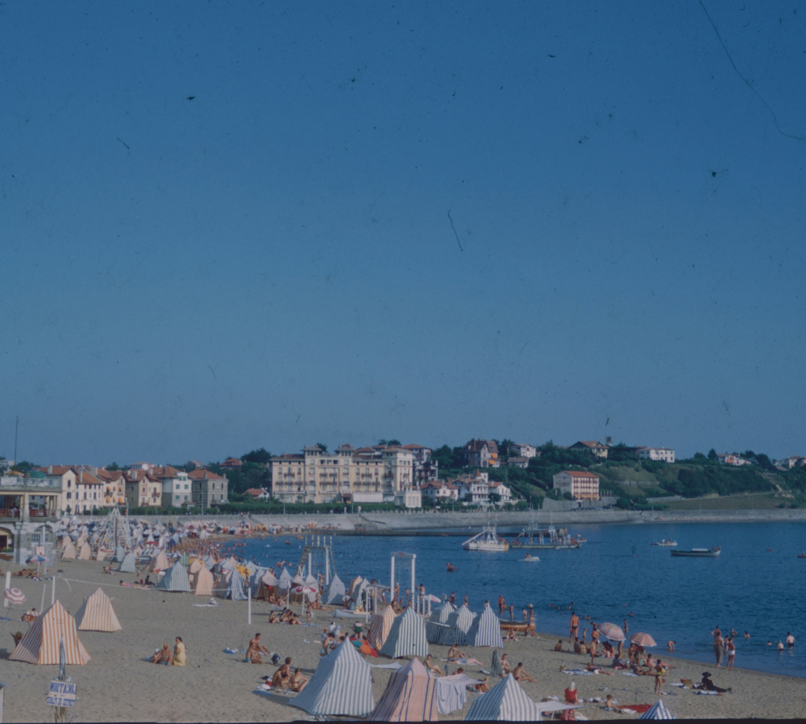 A crowded beach with striped tents and people along the coast of Saint-Jean-de-Luz