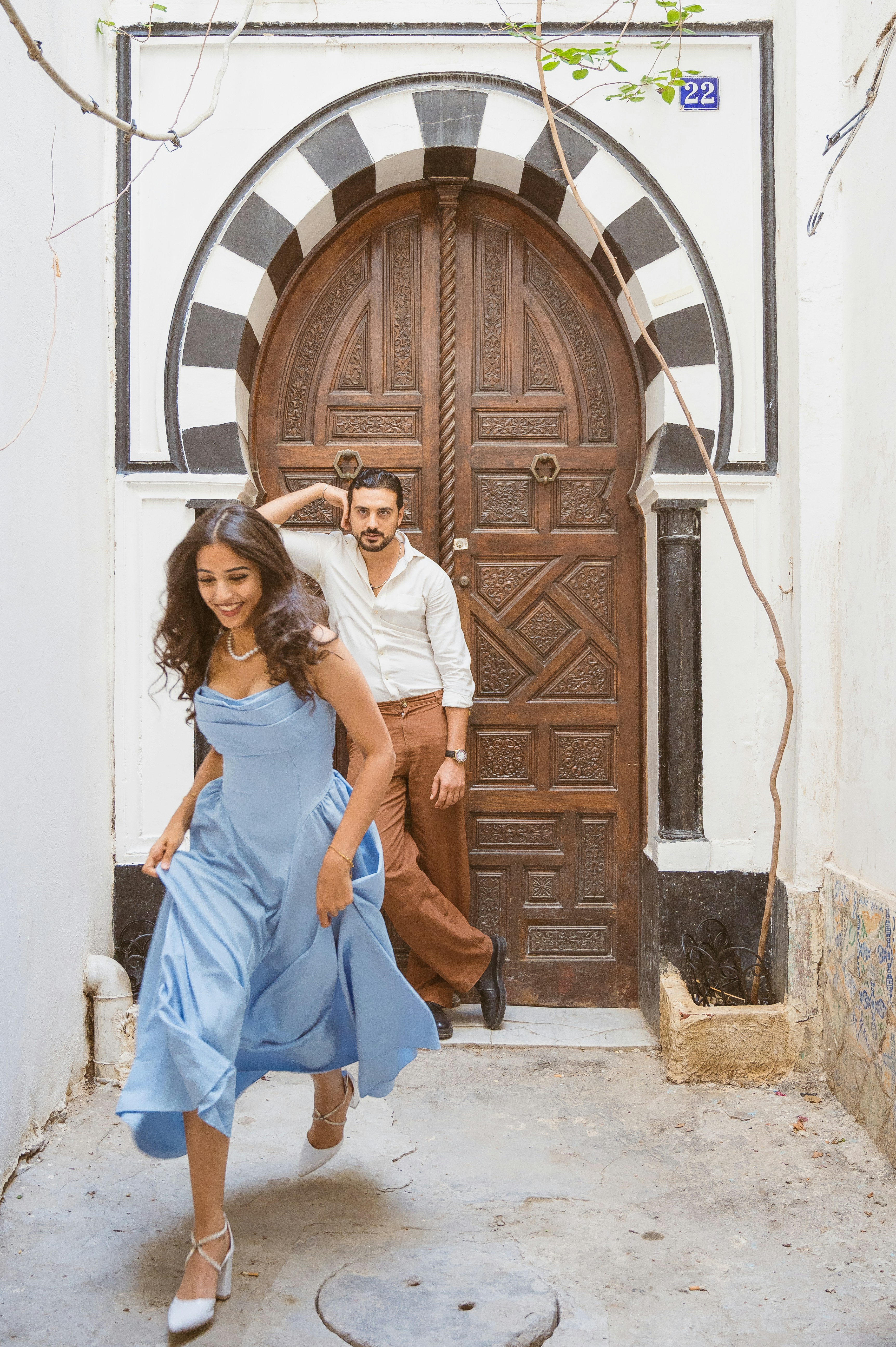 A woman in a blue dress walking past a man leaning against a wooden door
