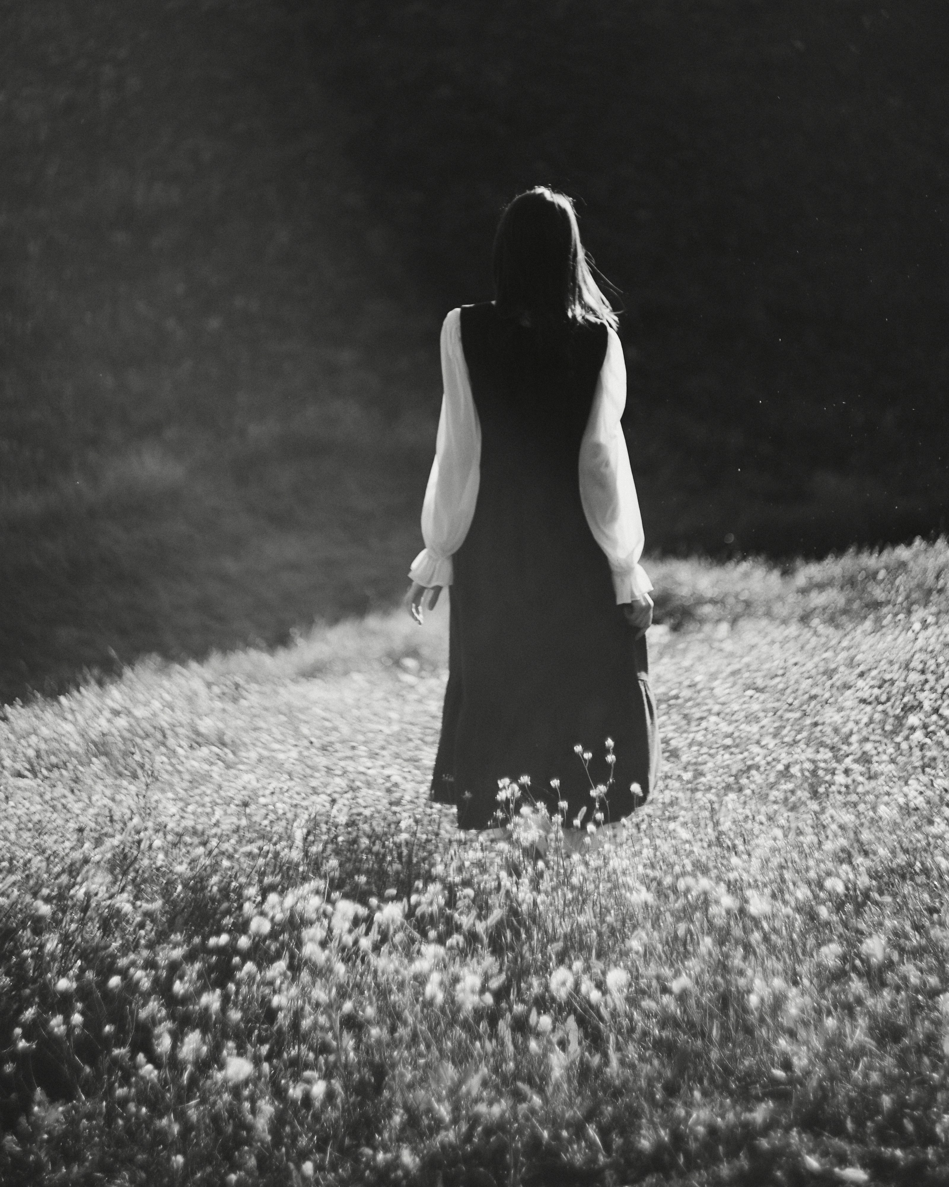 A woman in a long dress walking through a field of wildflowers in black and white