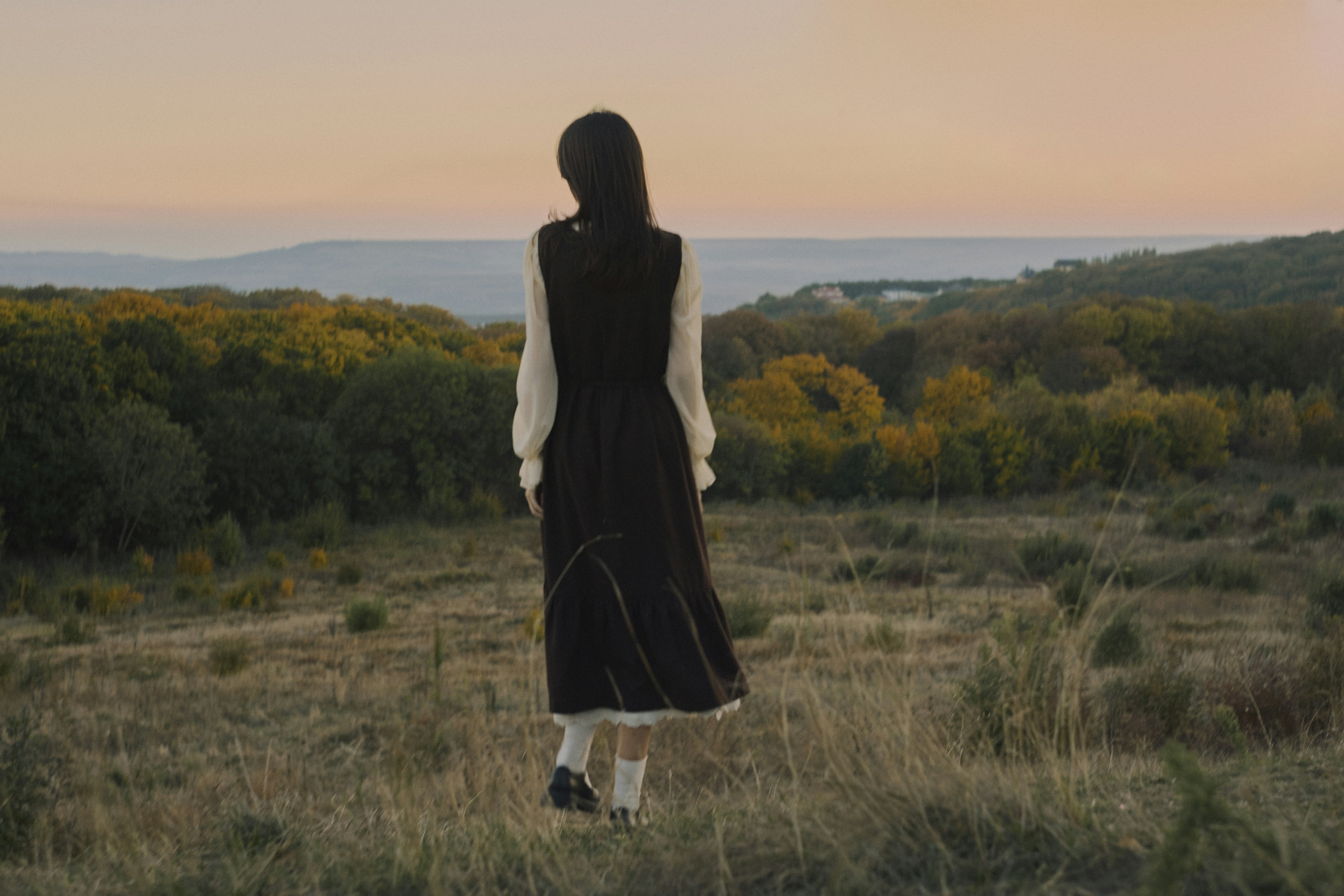 A woman in a dark dress and white sleeves standing in a field at golden hour