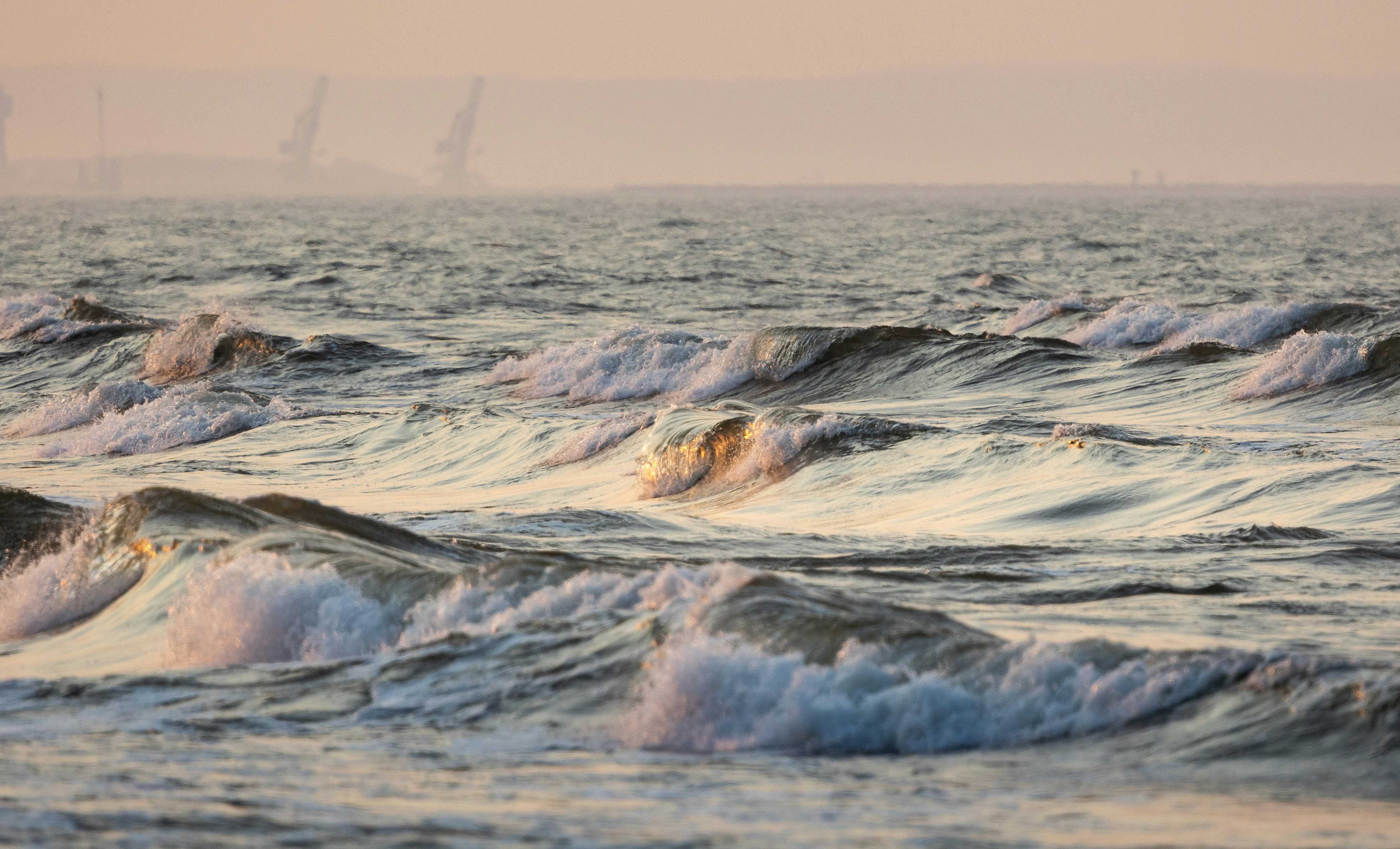 Rolling ocean waves with golden light reflecting on the water under a hazy sky