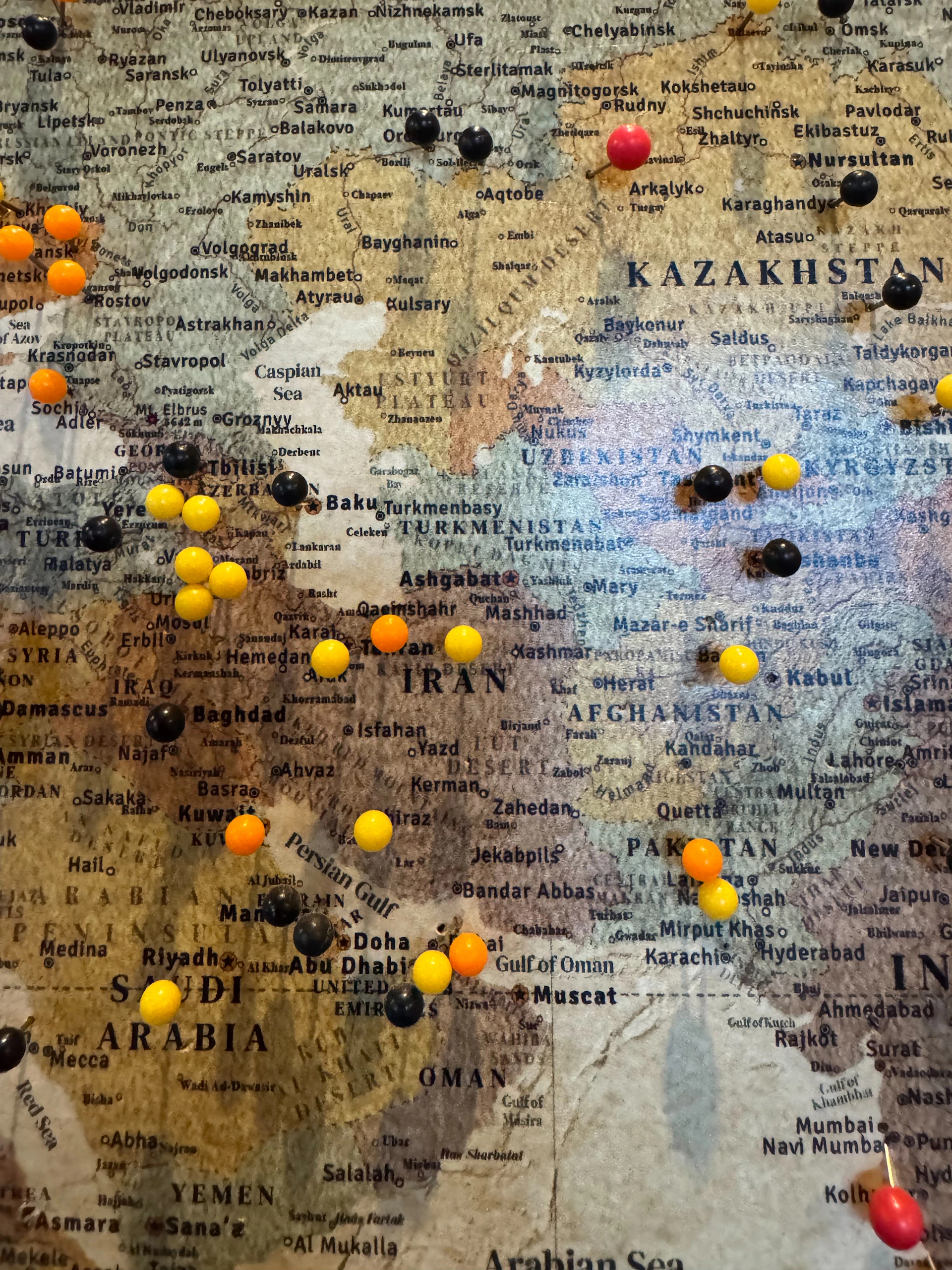 A vintage world map with colorful push pins marking various locations across the Middle East and Central Asia