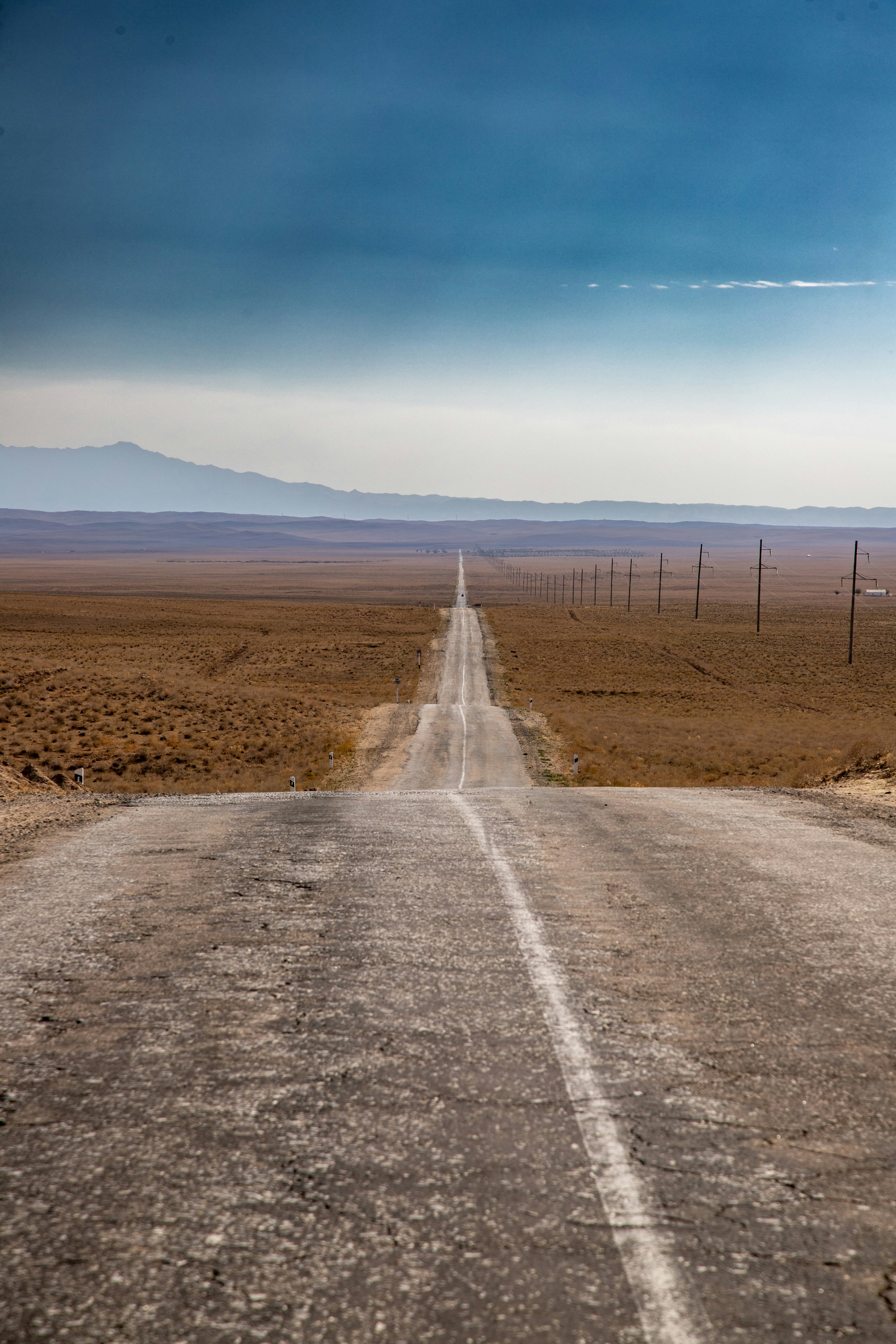 A long straight road stretching through a vast arid landscape toward distant mountains