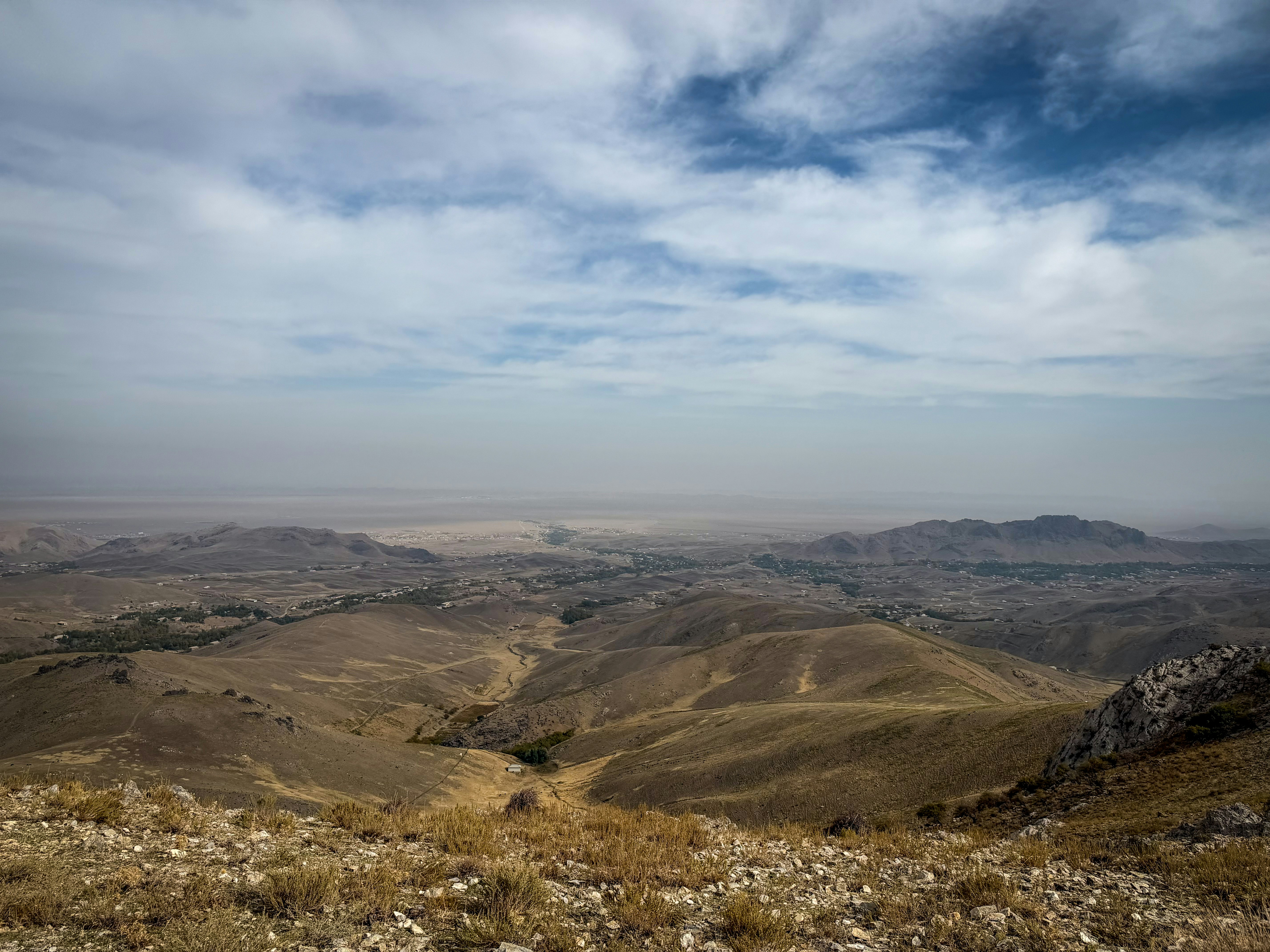 A vast landscape of rolling brown hills under a cloudy sky