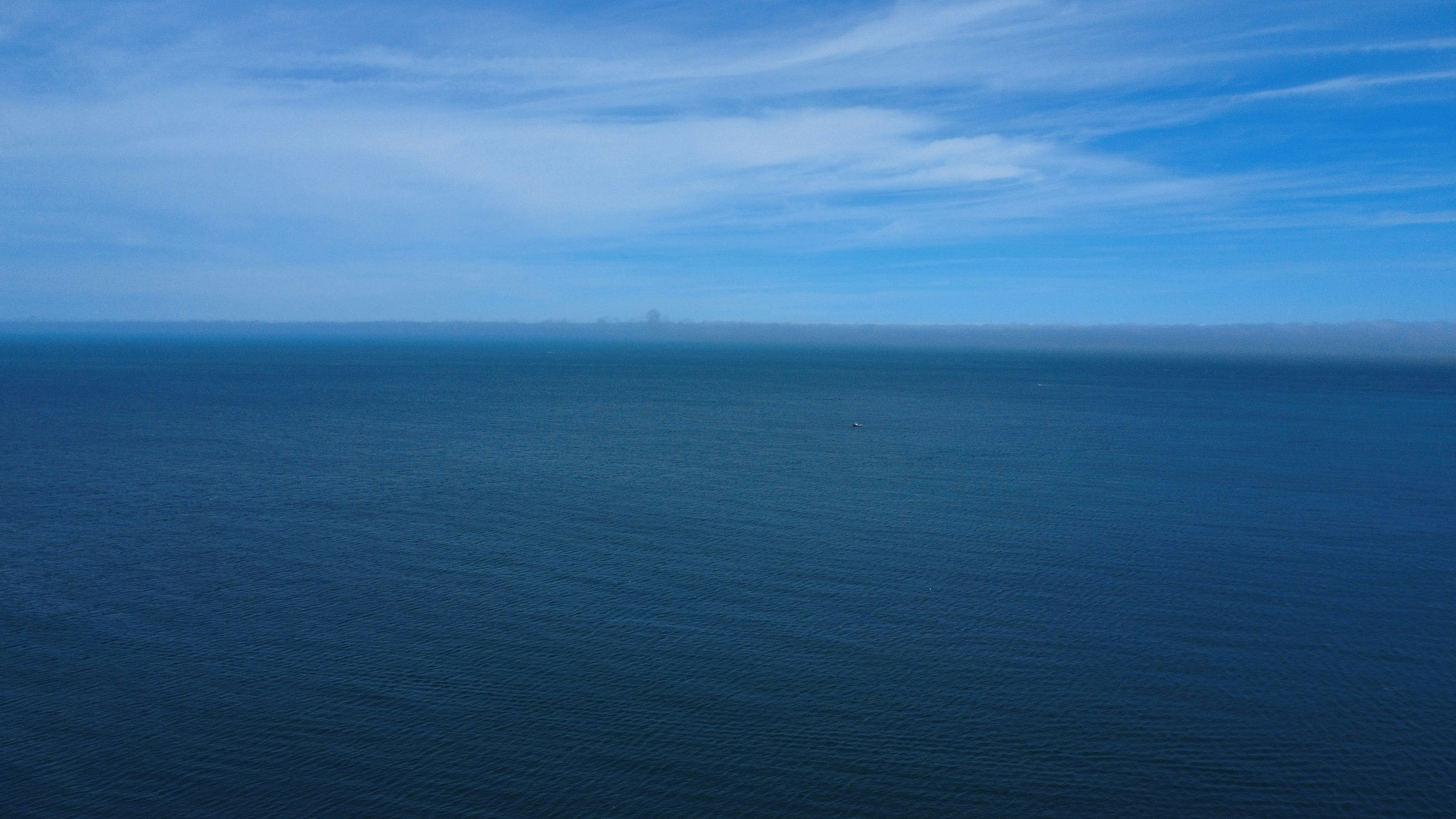 A vast blue ocean under a bright sky with a thin layer of distant fog