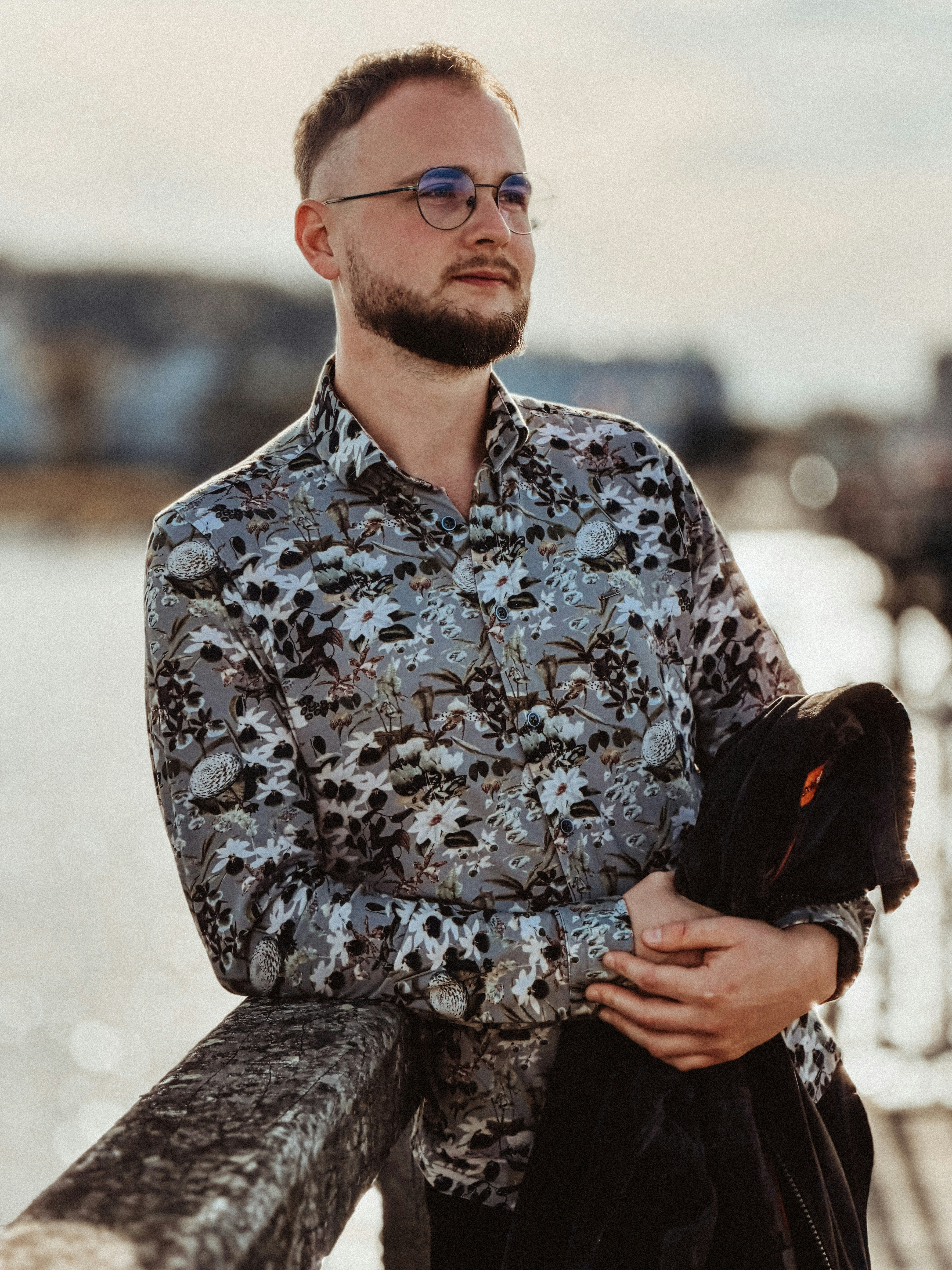 A man with a beard and glasses wearing a floral shirt leaning on a wooden railing