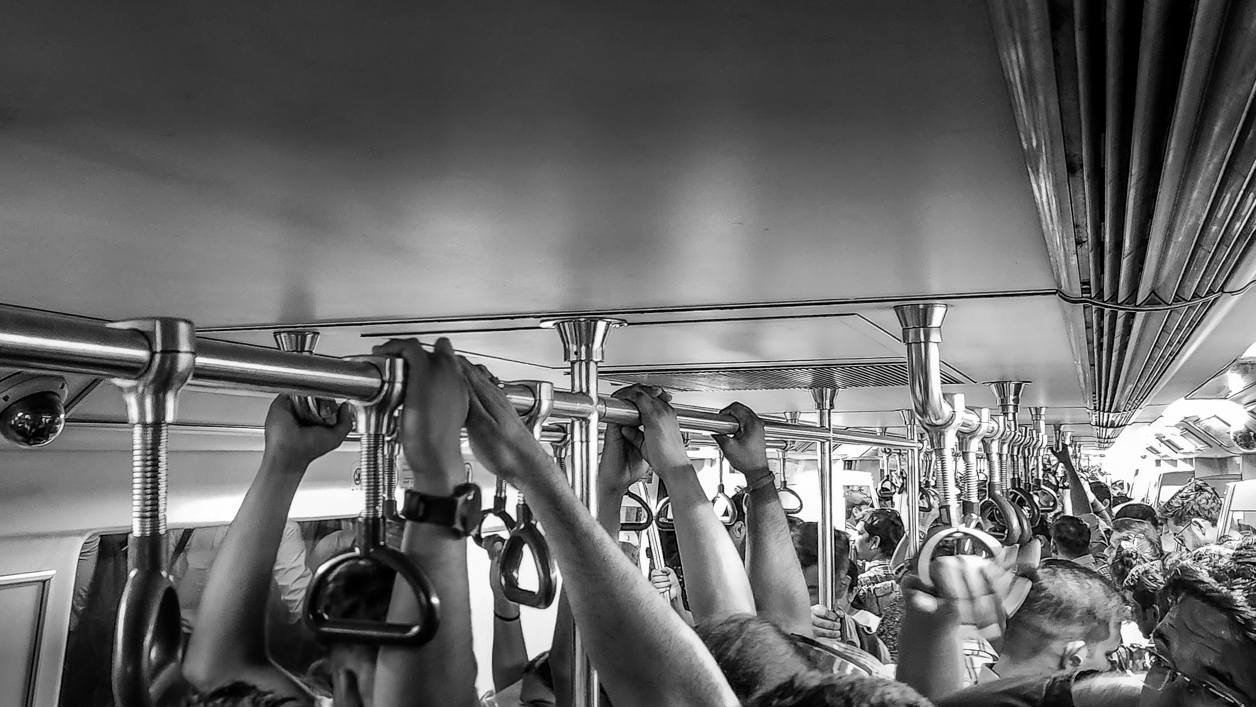 People holding onto overhead handles inside a crowded metro train in black and white