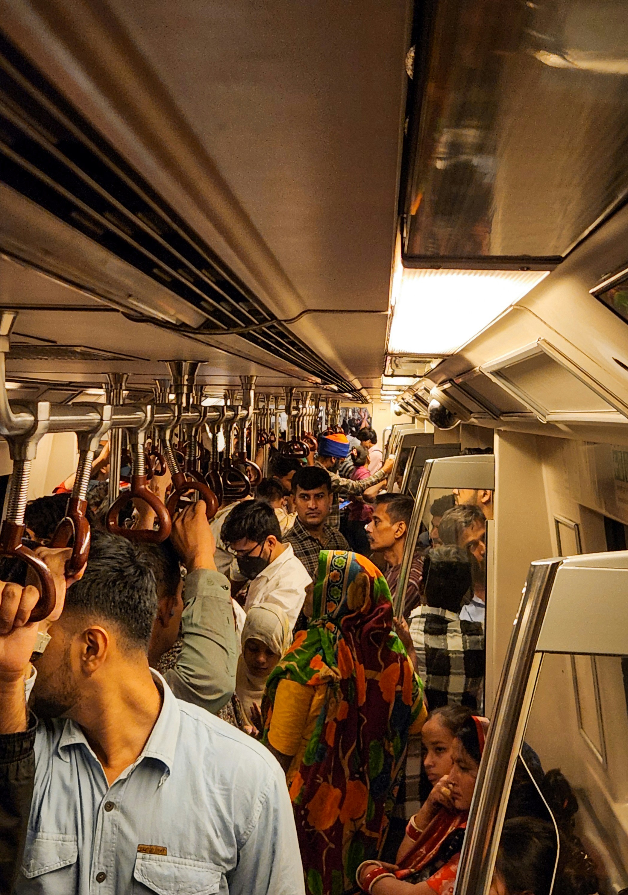 A crowded Delhi metro train carriage with many people standing and holding onto overhead handrails