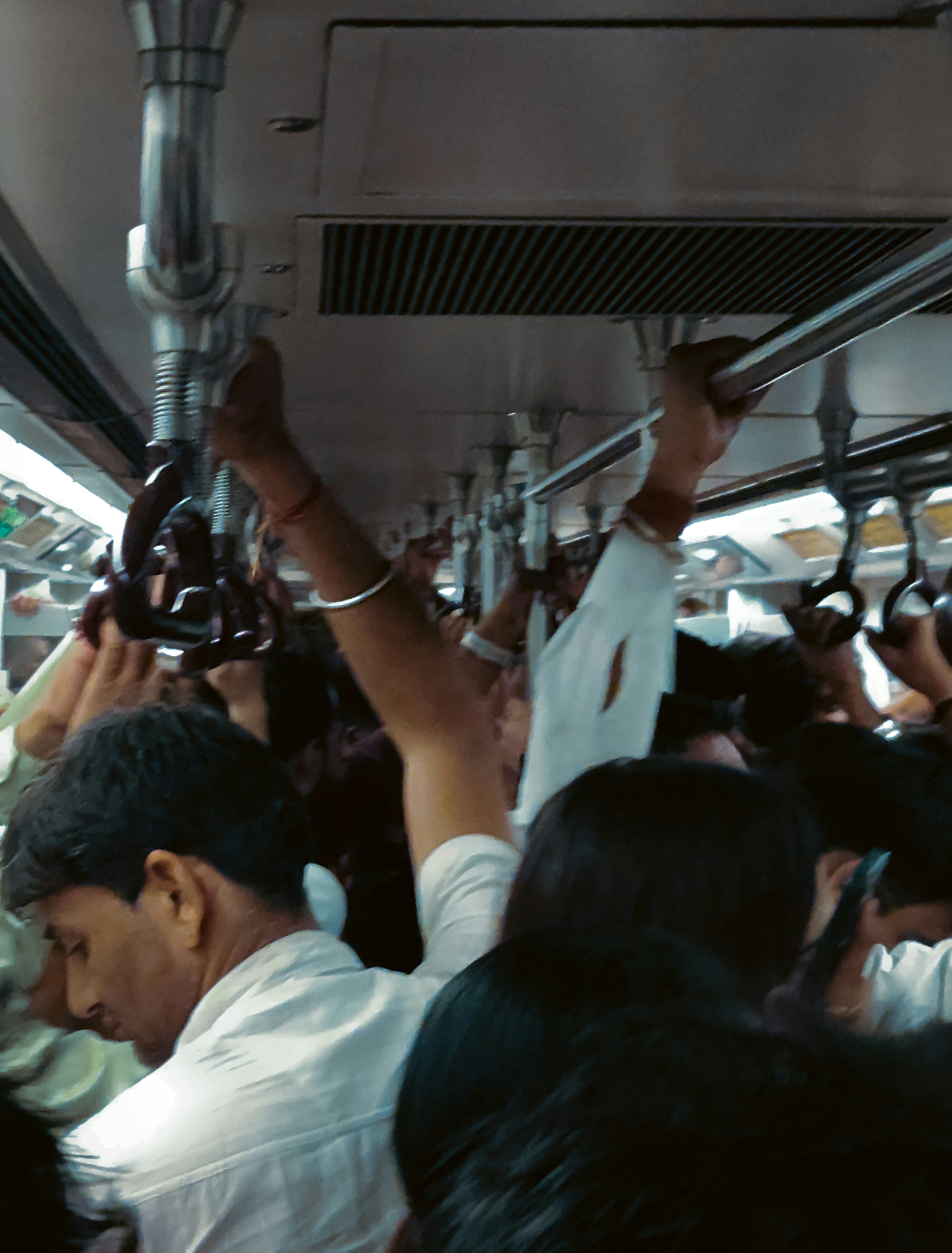 Commuters holding onto overhead handrails inside a crowded Delhi metro train