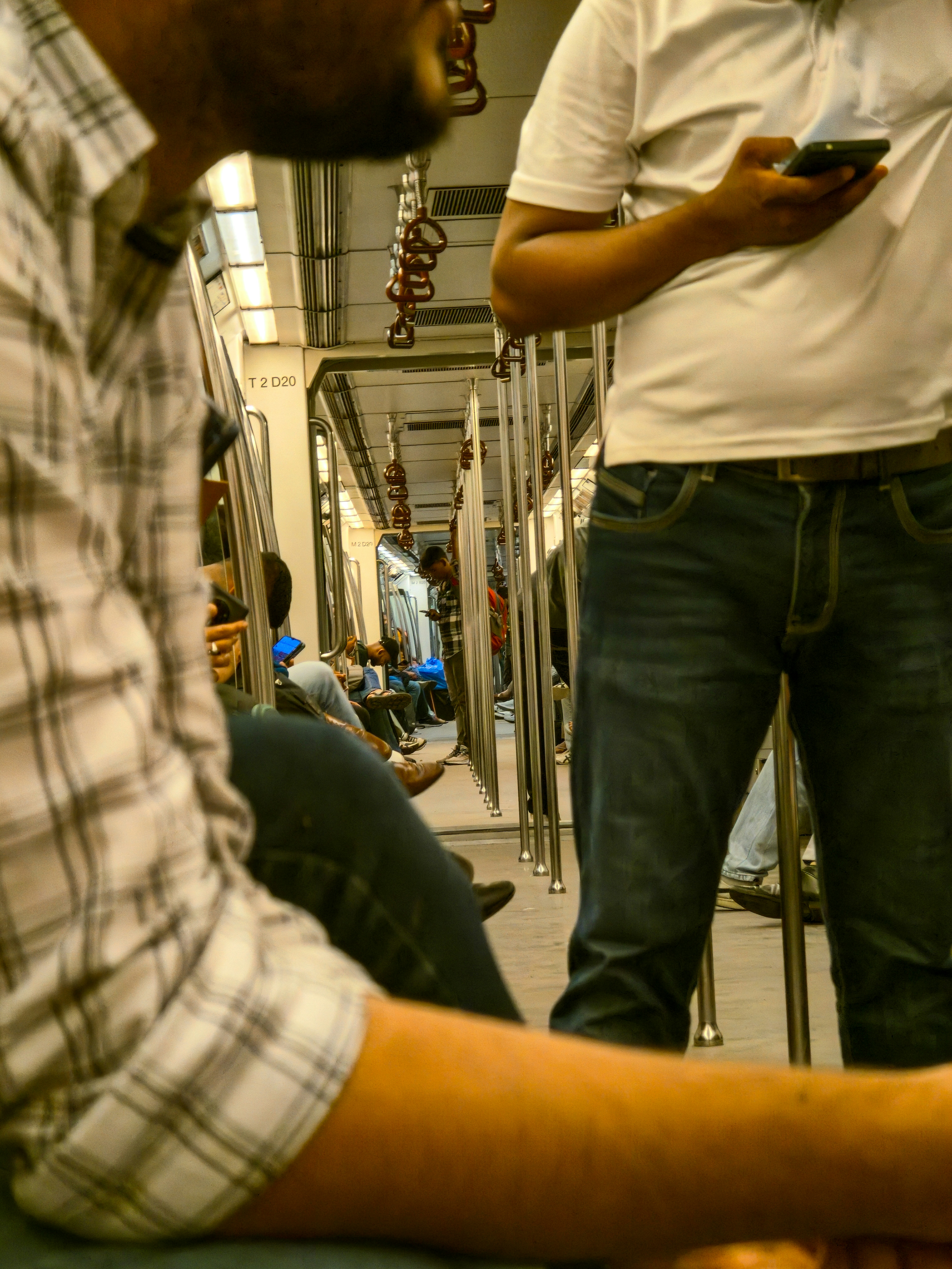 People seated and standing inside a Delhi metro train carriage with metal poles