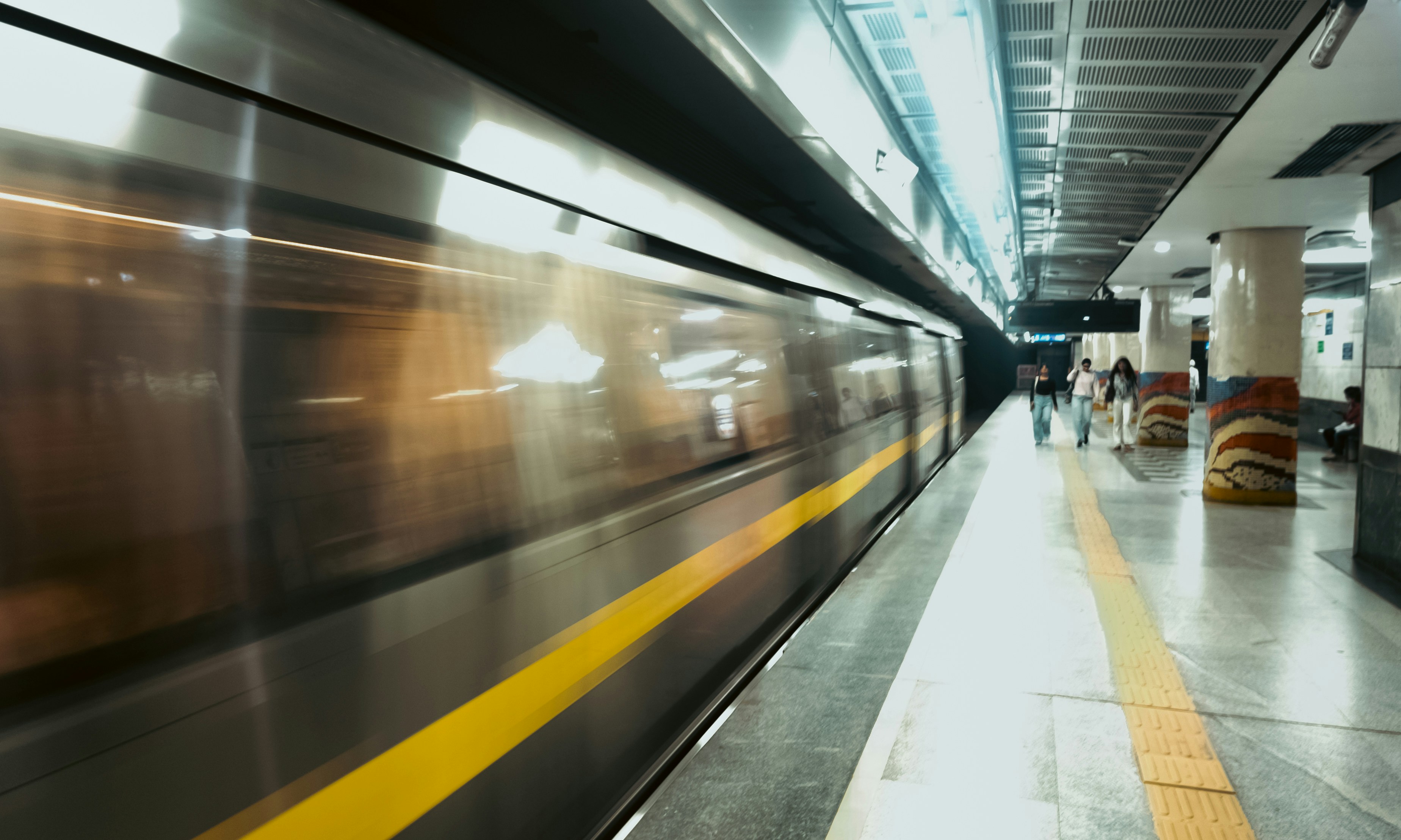 A motion-blurred metro train with a yellow stripe passing through a subway station
