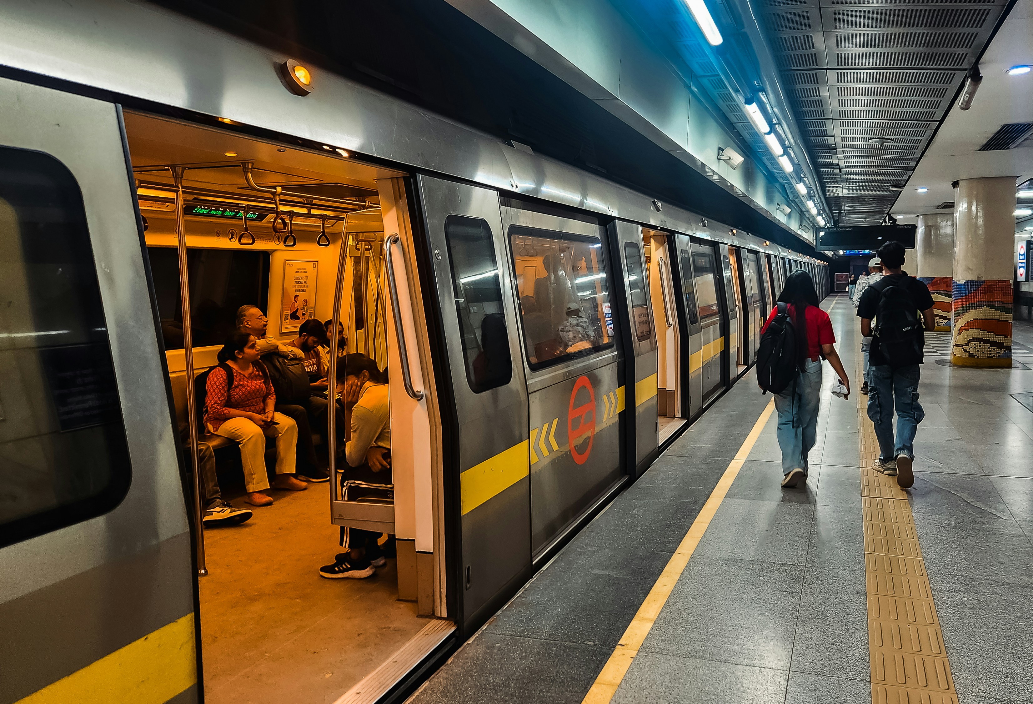 A Delhi Metro train with open doors at a station platform with commuters walking nearby