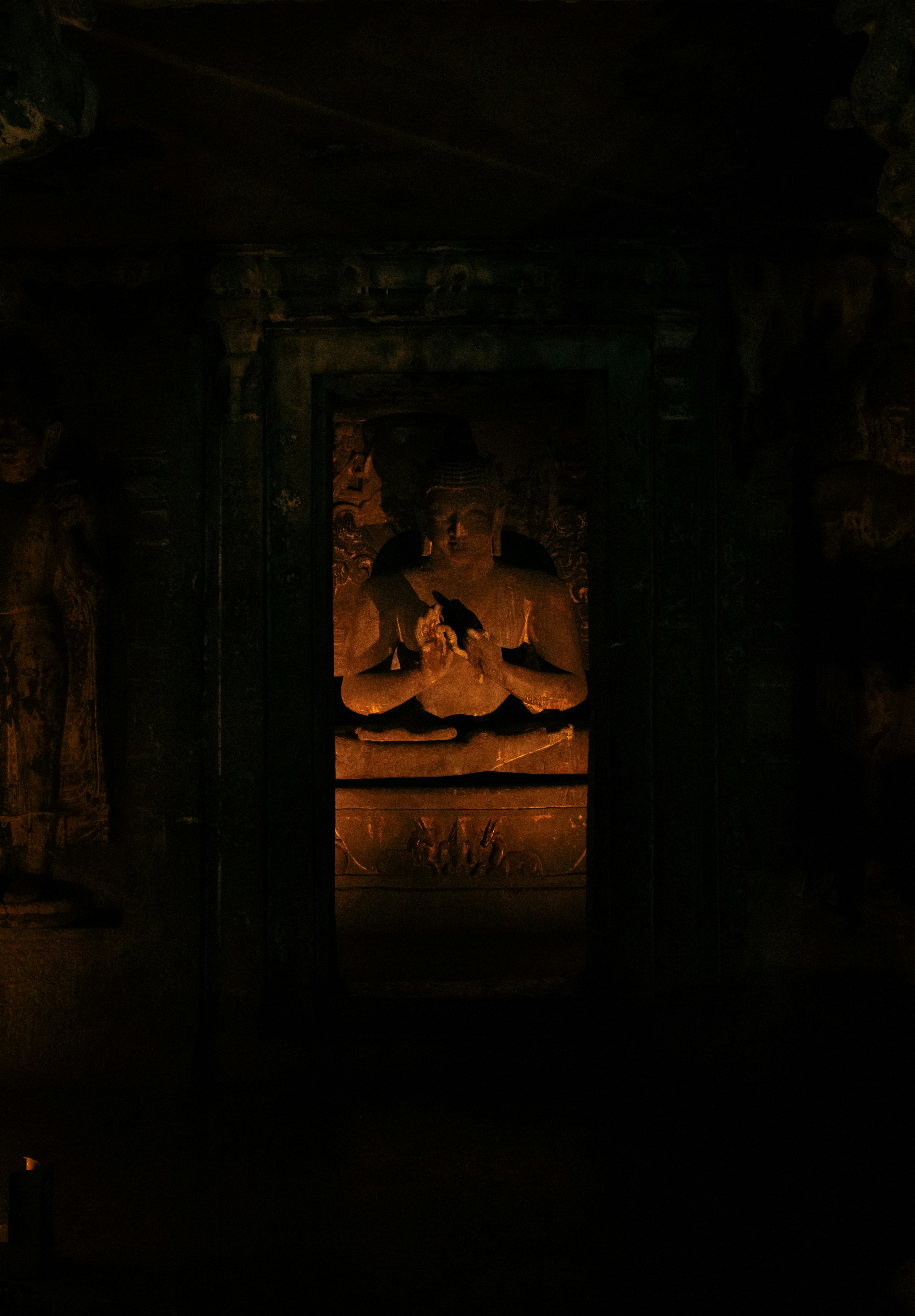 A seated Buddha statue carved into rock in the dim Ajanta Caves in Maharashtra, India