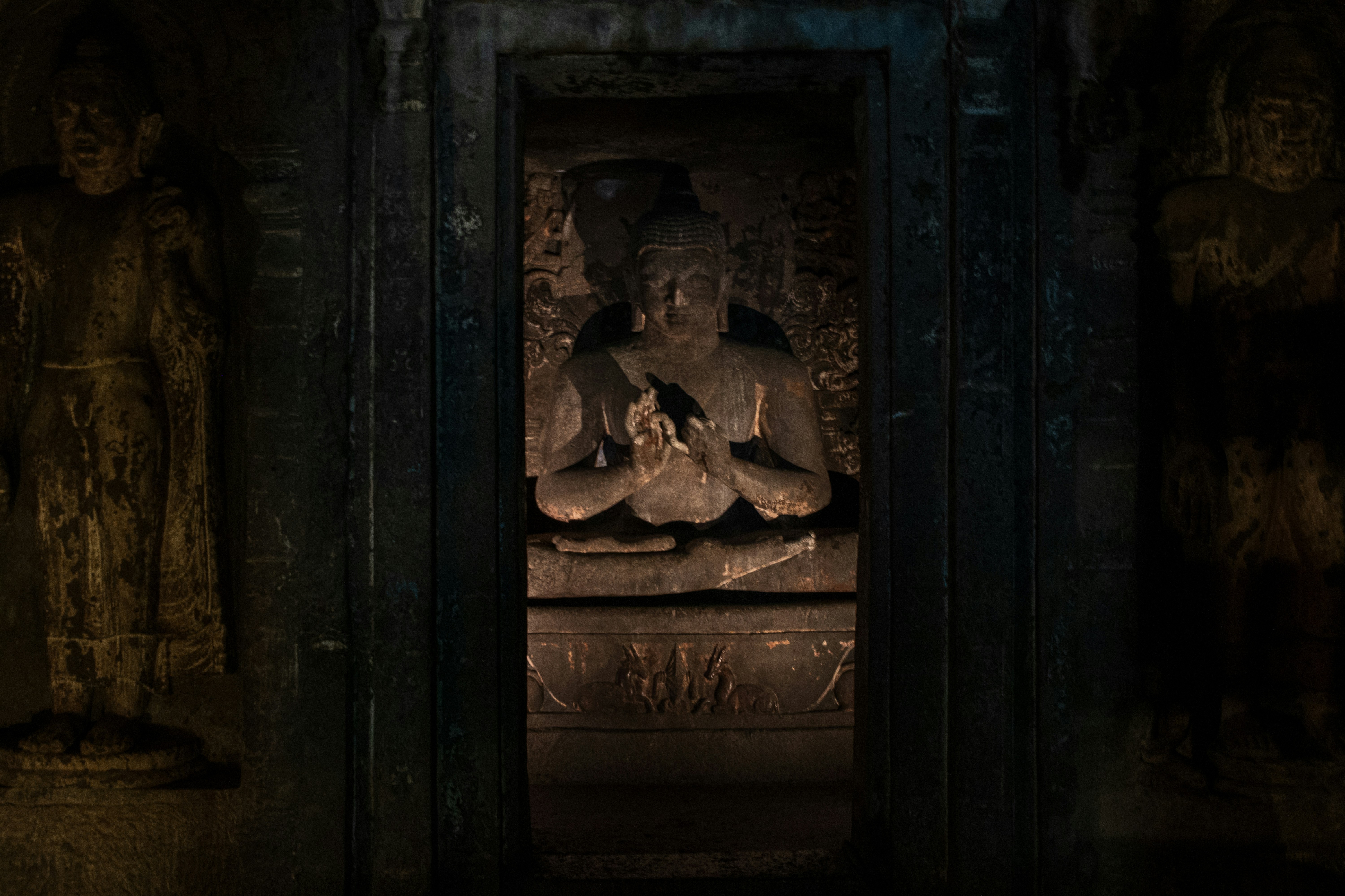 A seated Buddha statue carved into the rock inside a dark shrine at the Ajanta Caves