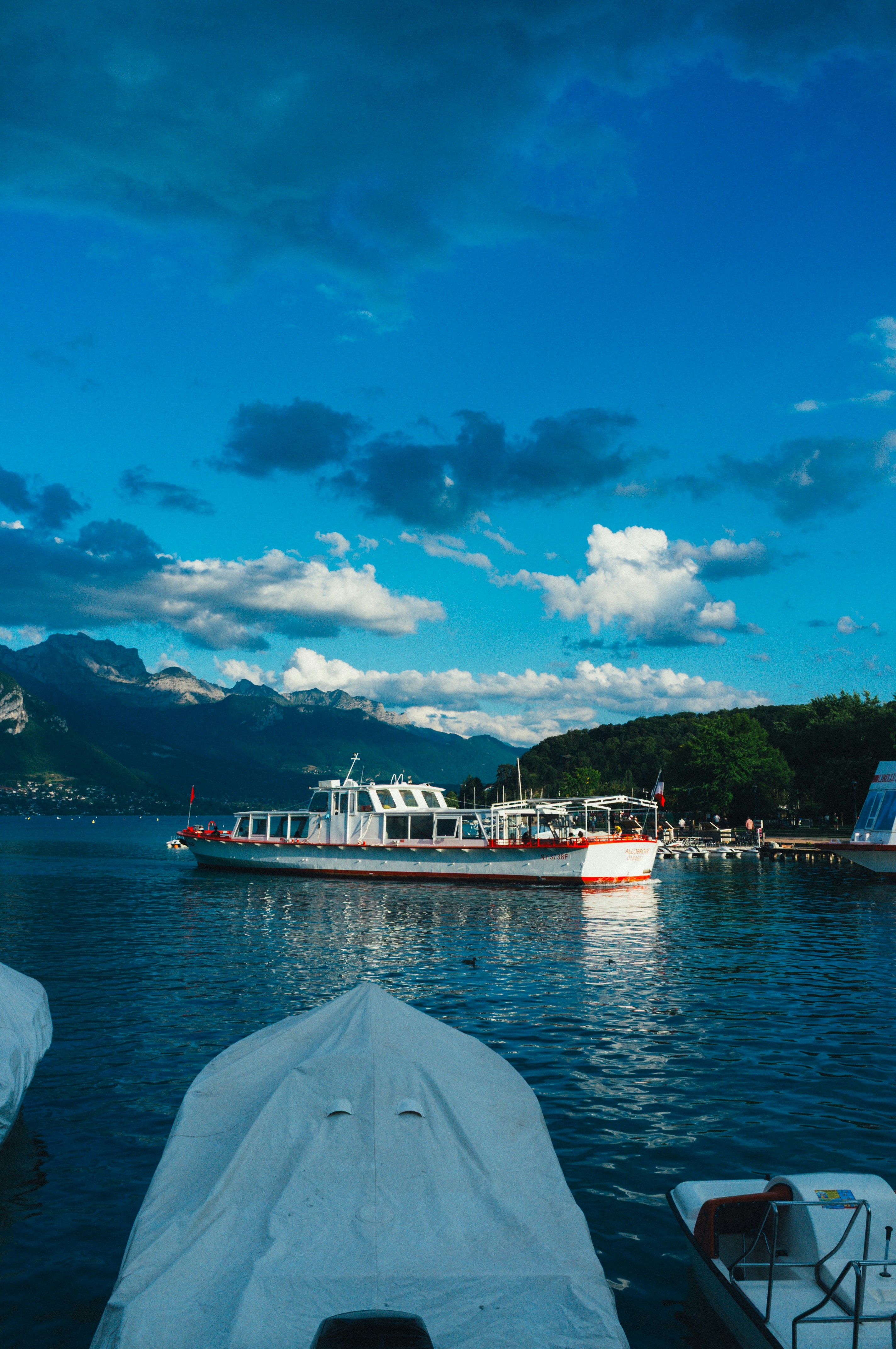 A white passenger boat on Lake Annecy with mountains in the background under a blue sky