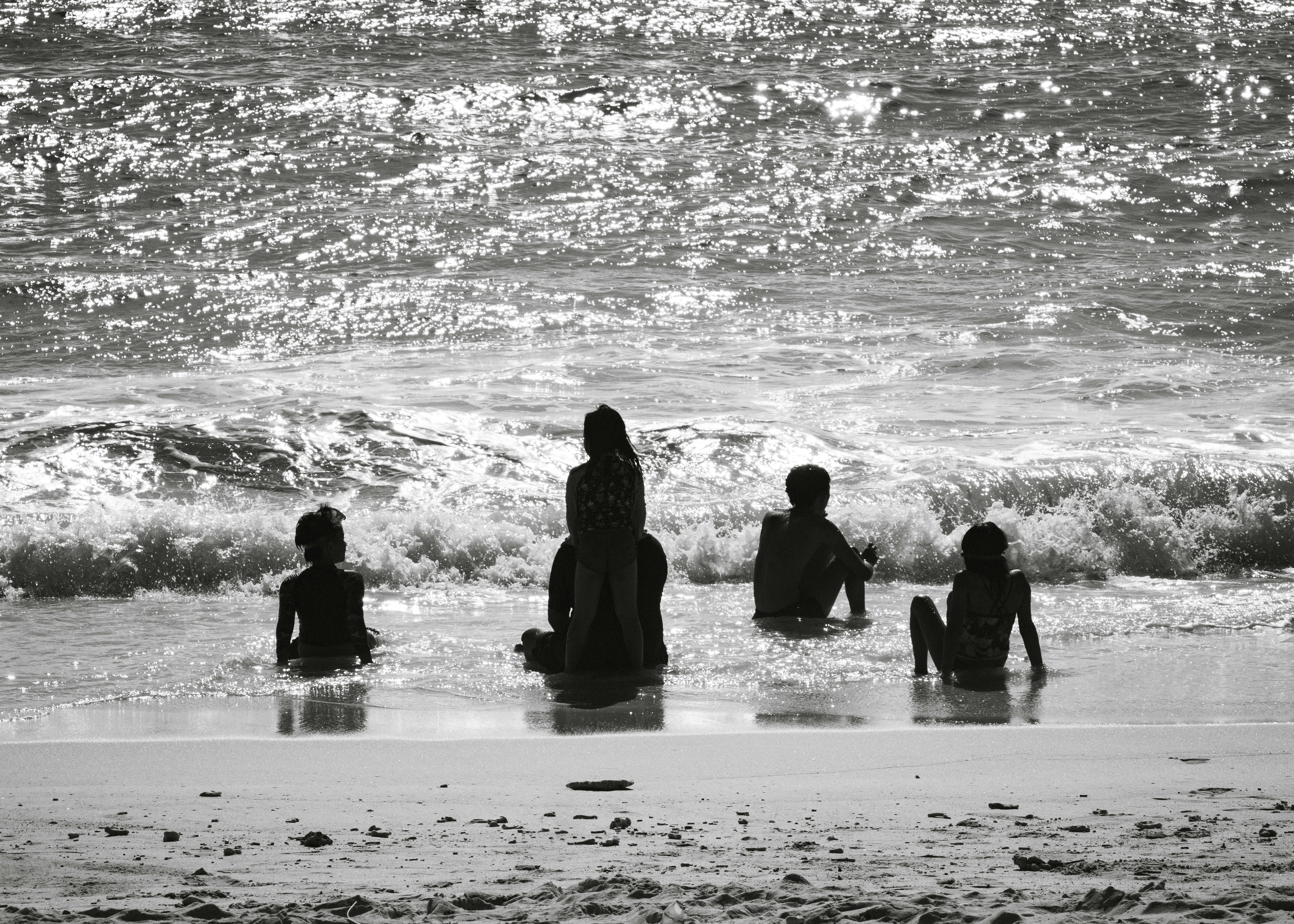 Silhouettes of a family sitting in the shallow surf on a bright sunny beach