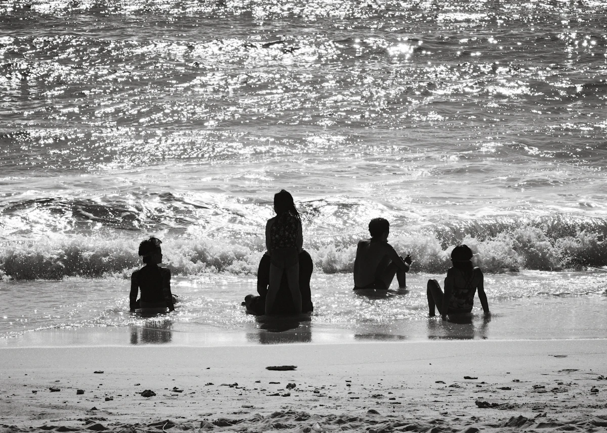 Siluet sebuah keluarga duduk di ombak dangkal pantai yang cerah