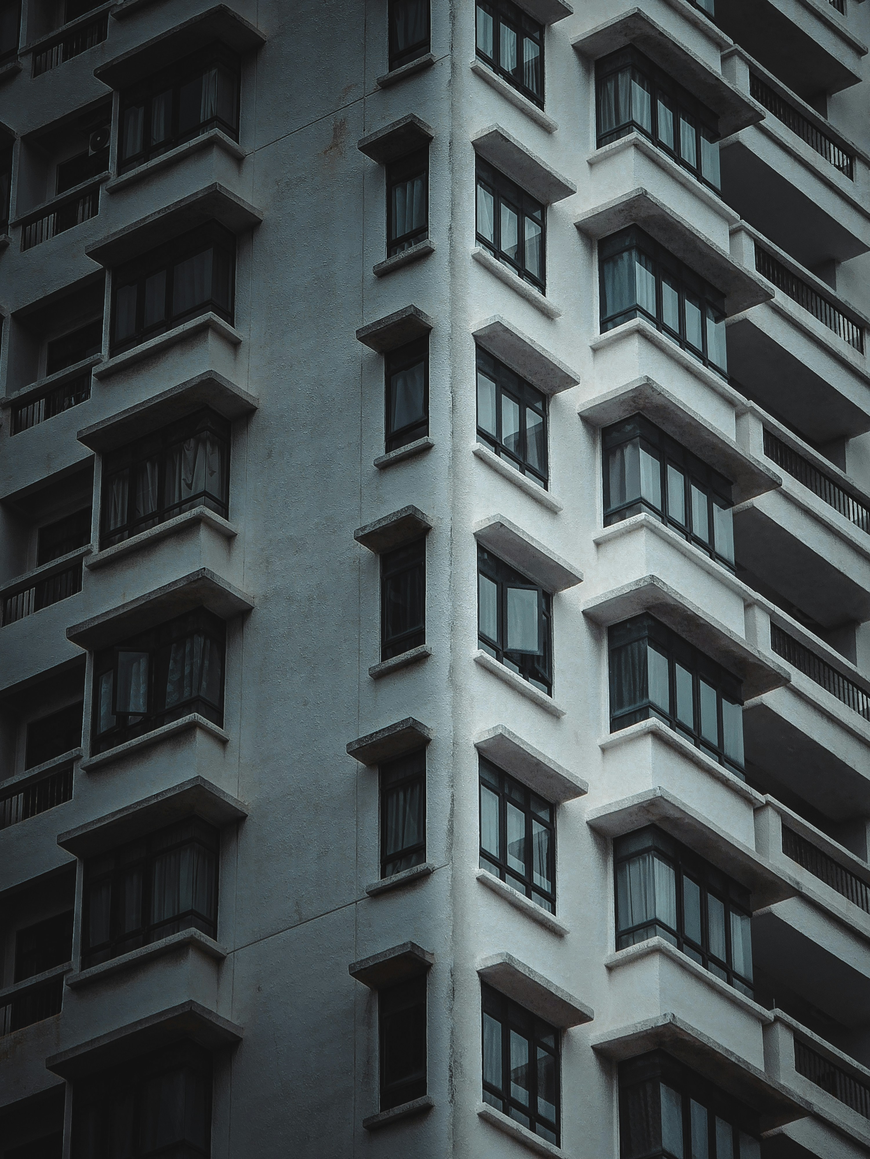 The corner of a tall white apartment building with rows of dark windows and concrete balconies